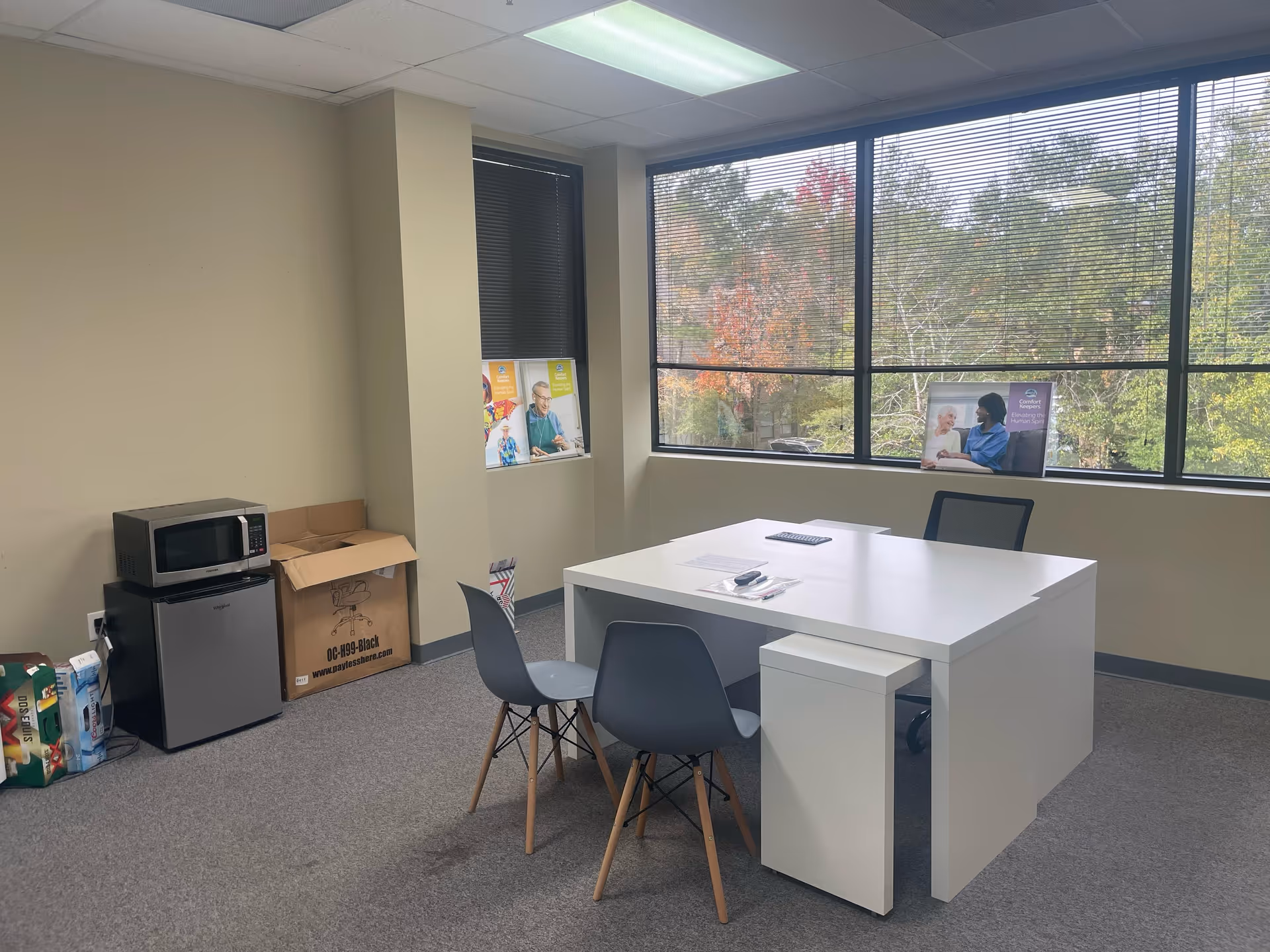 Small office area with a white desk, chairs, large windows, and a microwave in corner.