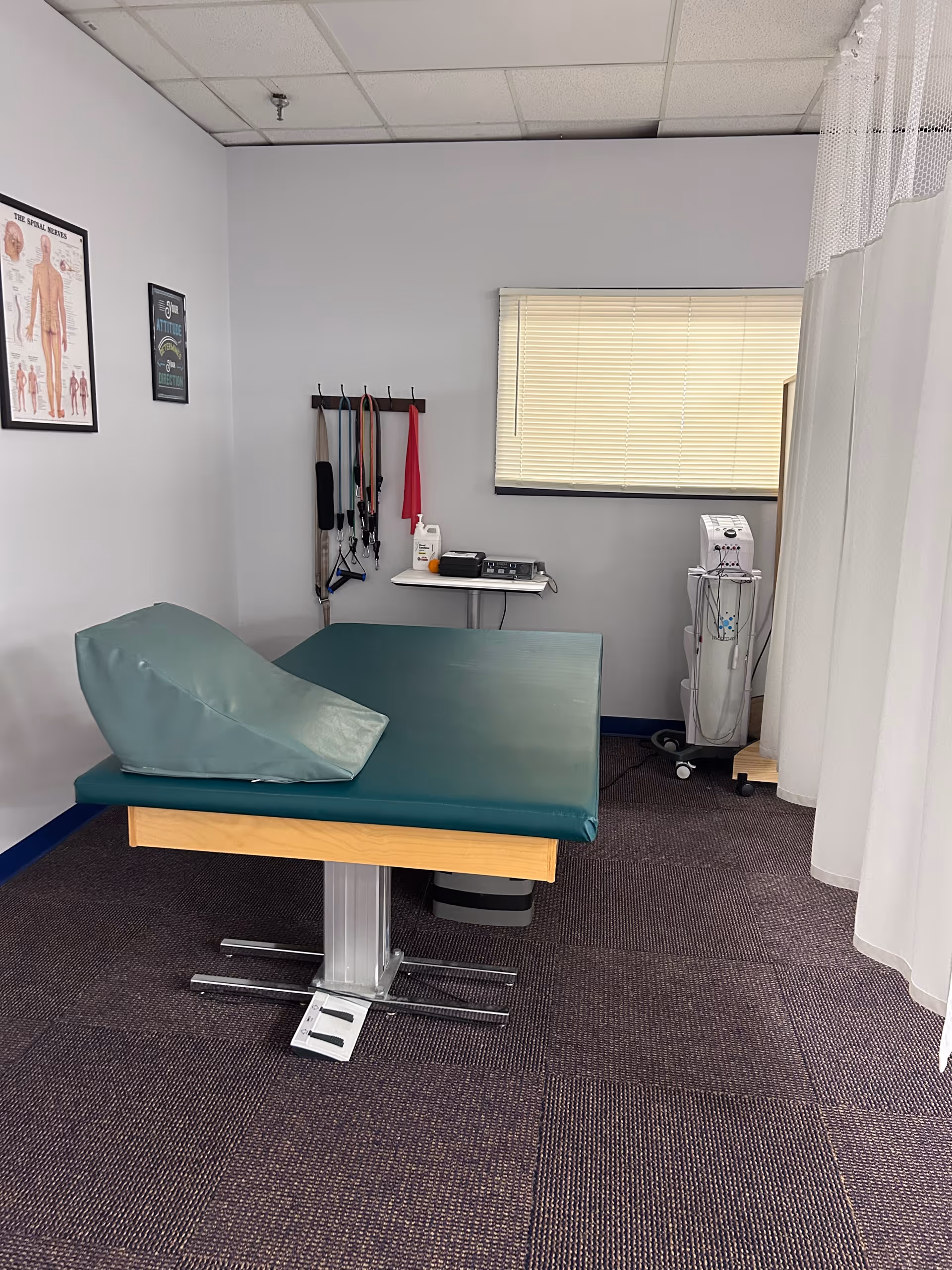 Examination table in a small physical therapy room with equipment and a curtain.