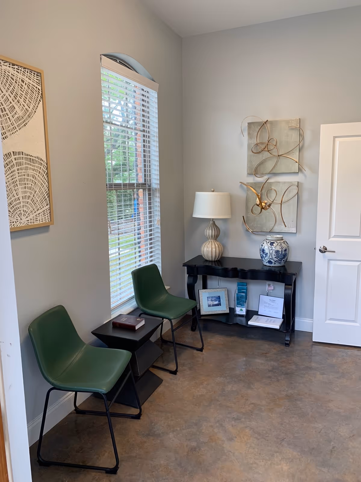 Small interior waiting area with two green chairs, a window, and a decorative console table.