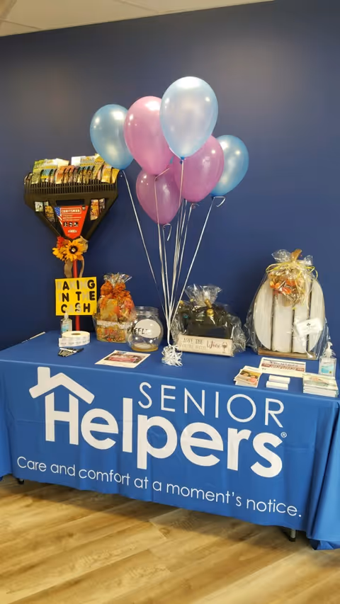 Indoor promotional table for Senior Helpers with balloons and gift baskets.