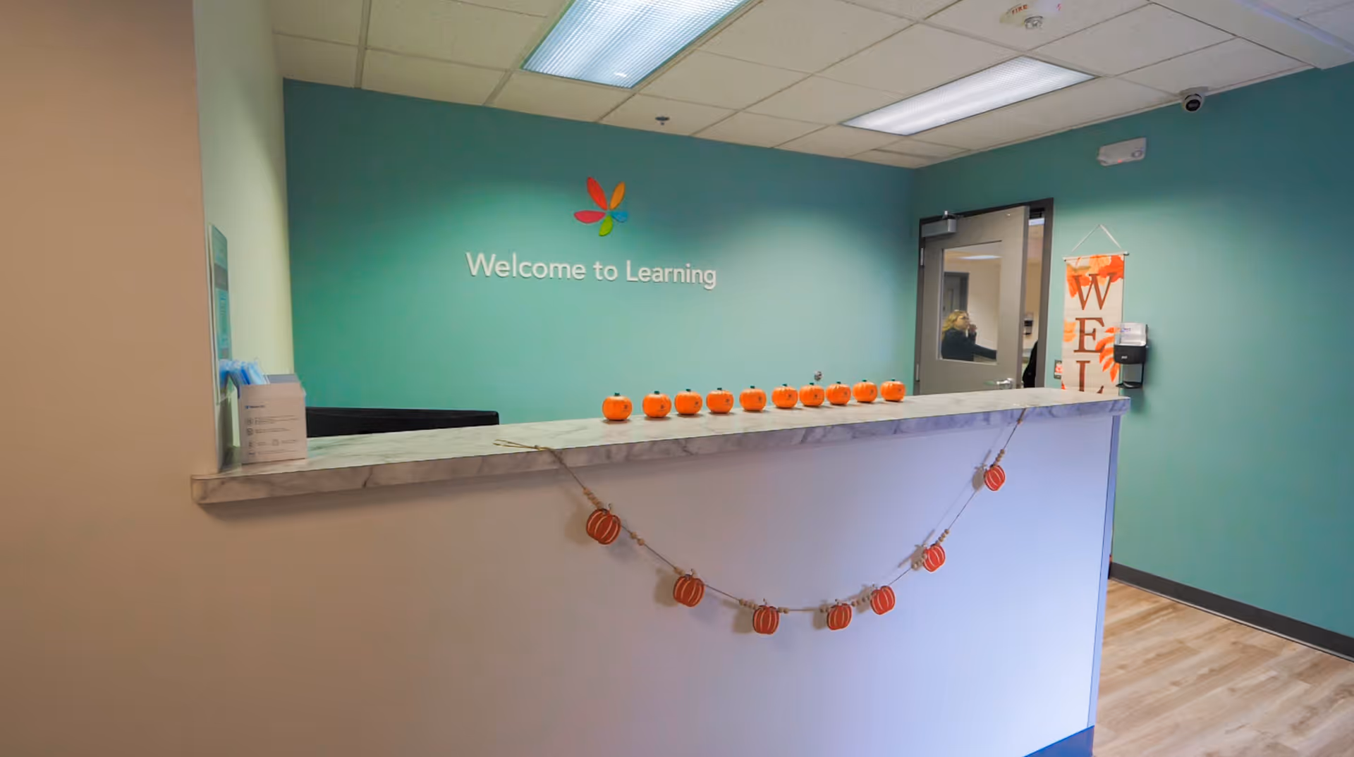 Indoor reception area with teal wall, marble counter, and pumpkin garland.
