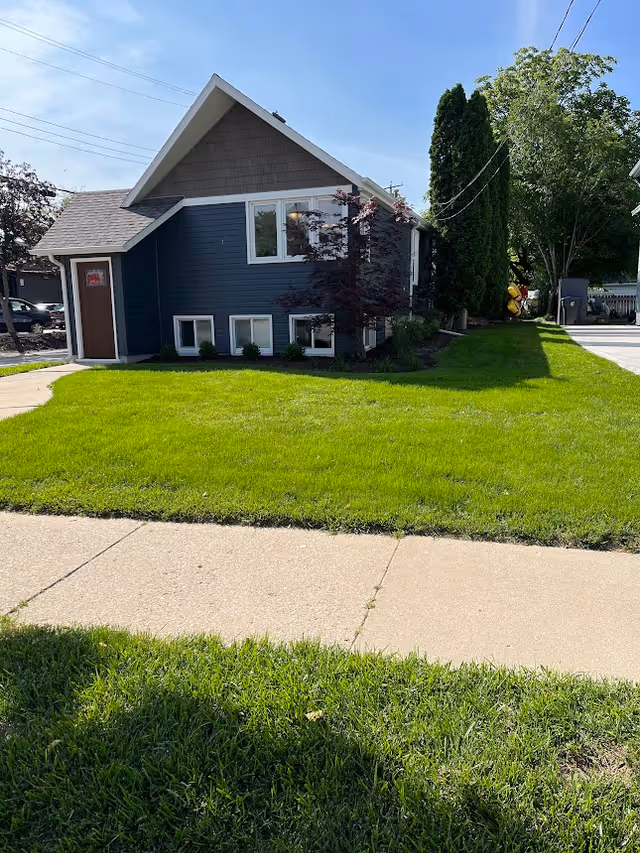 Blue two-story house with sloped roof, manicured lawn, and sidewalk.