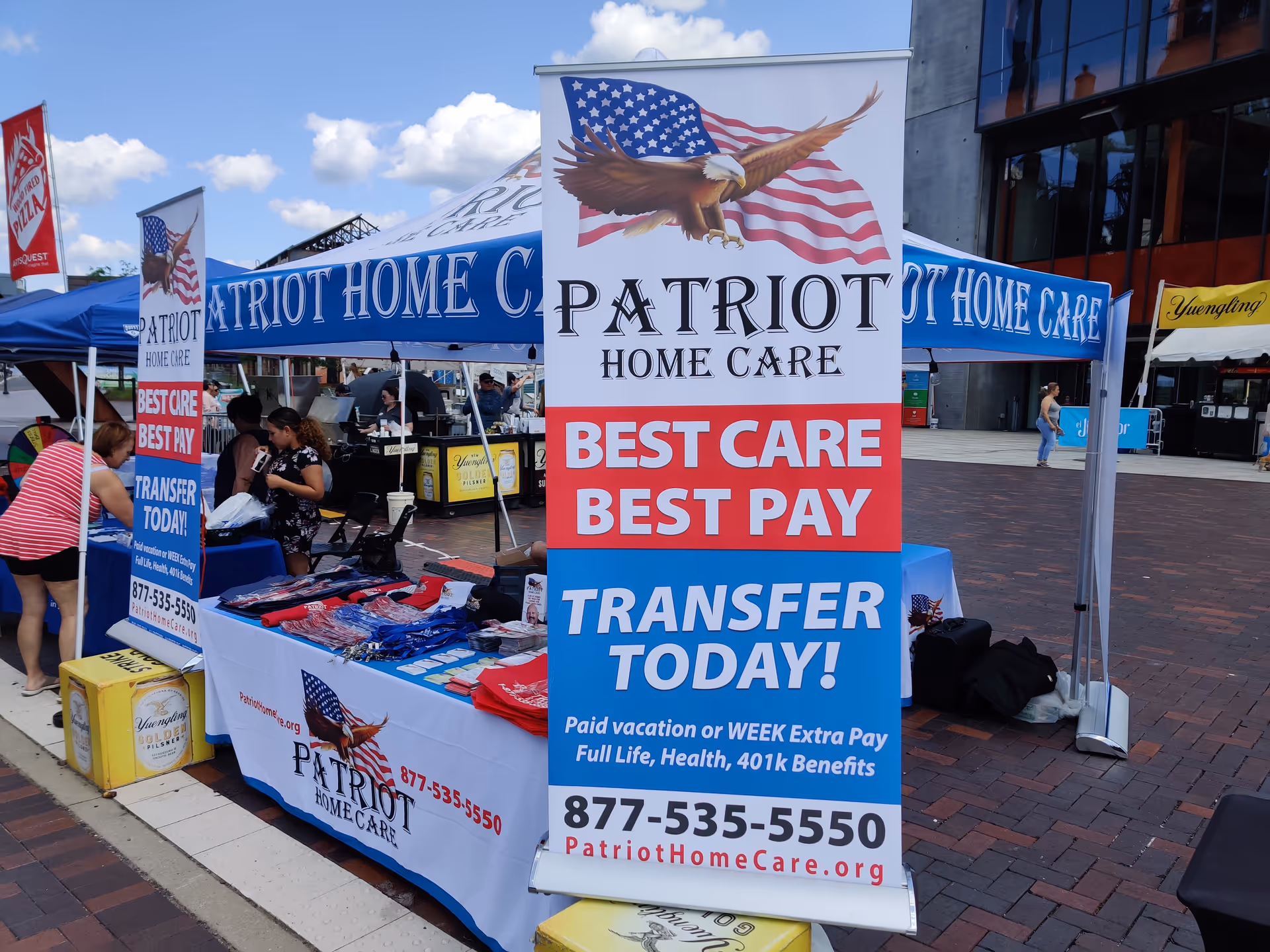 Outdoor Patriot Home Care booth with banners, tents, and people at a street event.