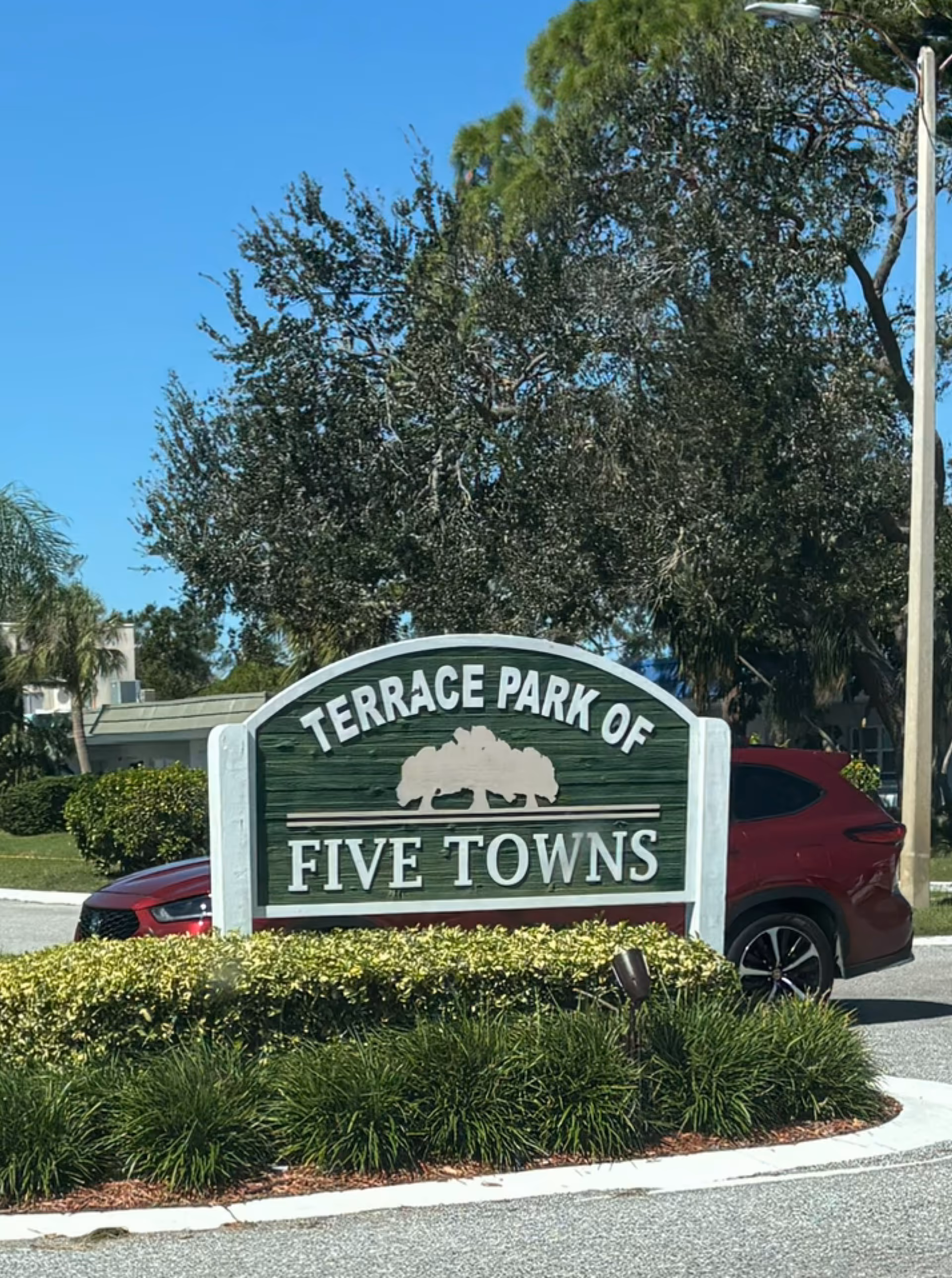 Exterior sign for Terrace Park of Five Towns with landscaping and a car.