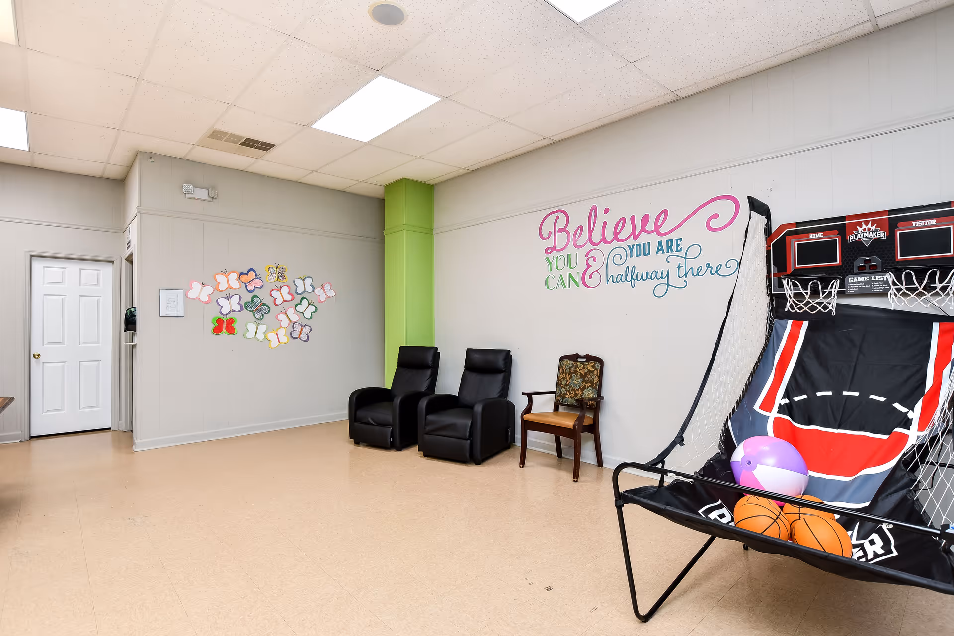 Indoor recreation room with wall quote, butterfly decor, chairs, and a basketball hoop setup.