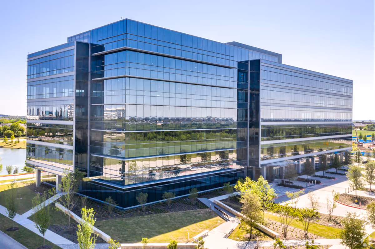 A modern glass office building with reflective facade and landscaped pathways.