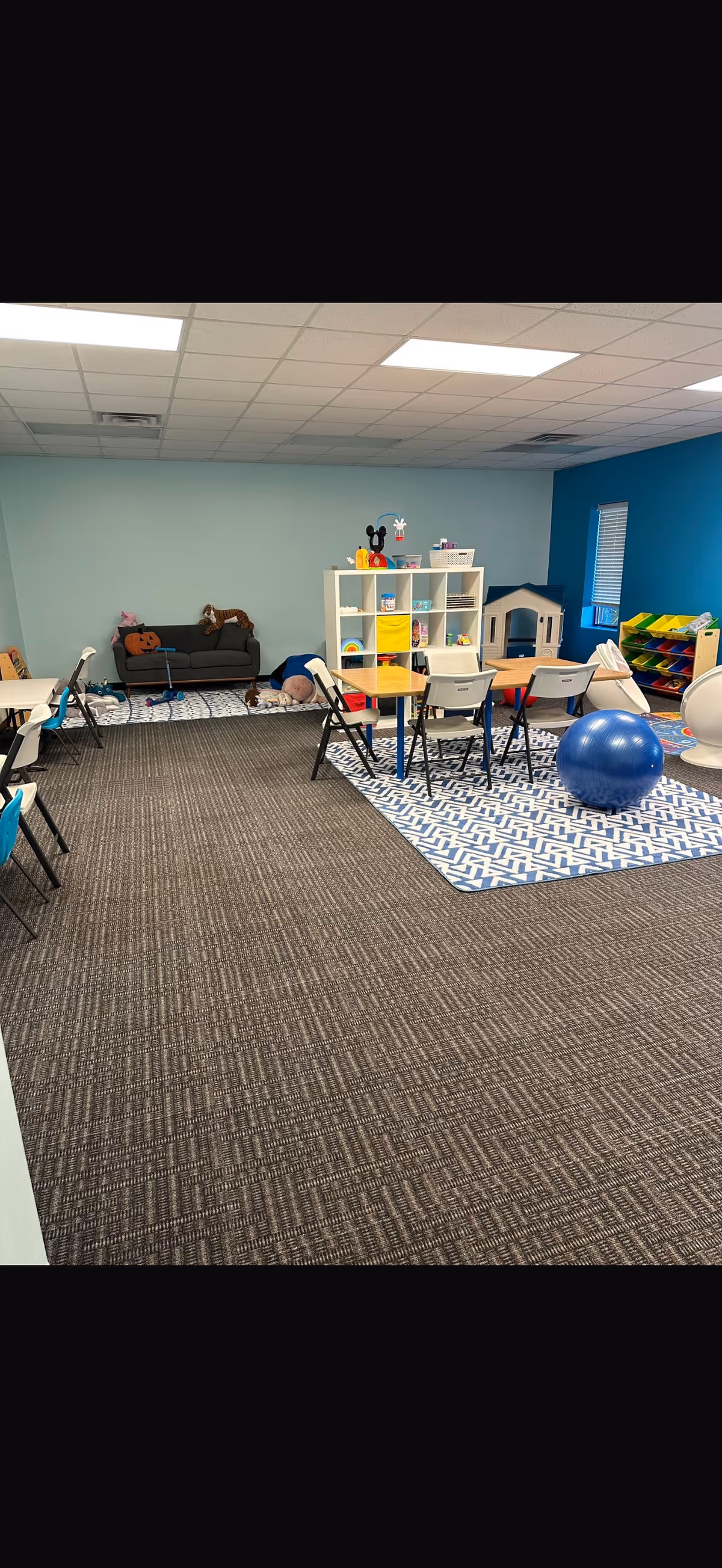 Colorful indoor playroom with toy shelves, small tables, and a blue exercise ball.