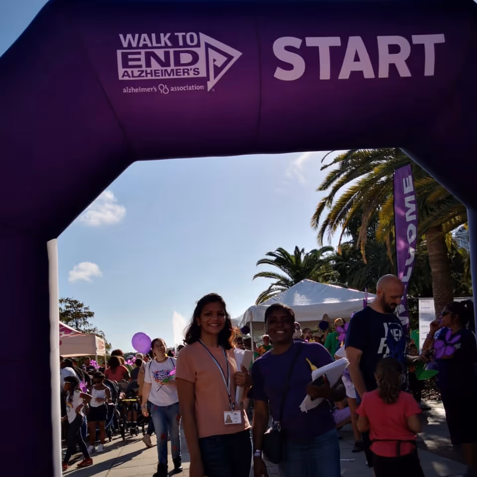 People participate in an outdoor Walk to End Alzheimer's event under a purple start arch.