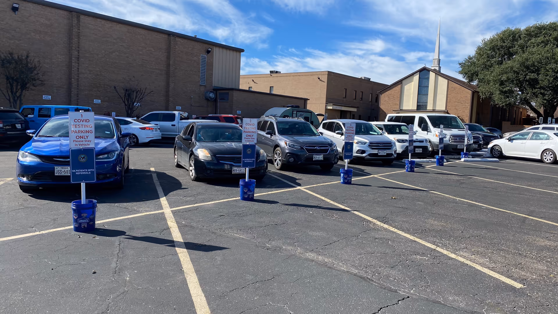 Outdoor parking lot with multiple cars in front of a brick facility.