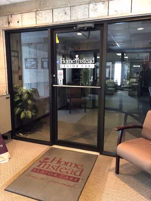 Glass doors with Home Instead Senior Care logo lead into a lobby with chairs and plants.