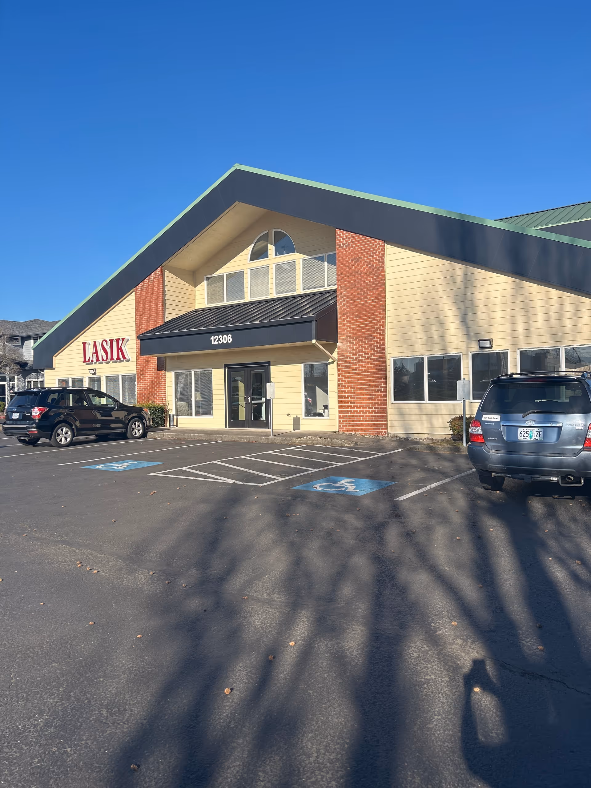 Exterior view of a beige building with green roof and LASIK sign in parking lot.