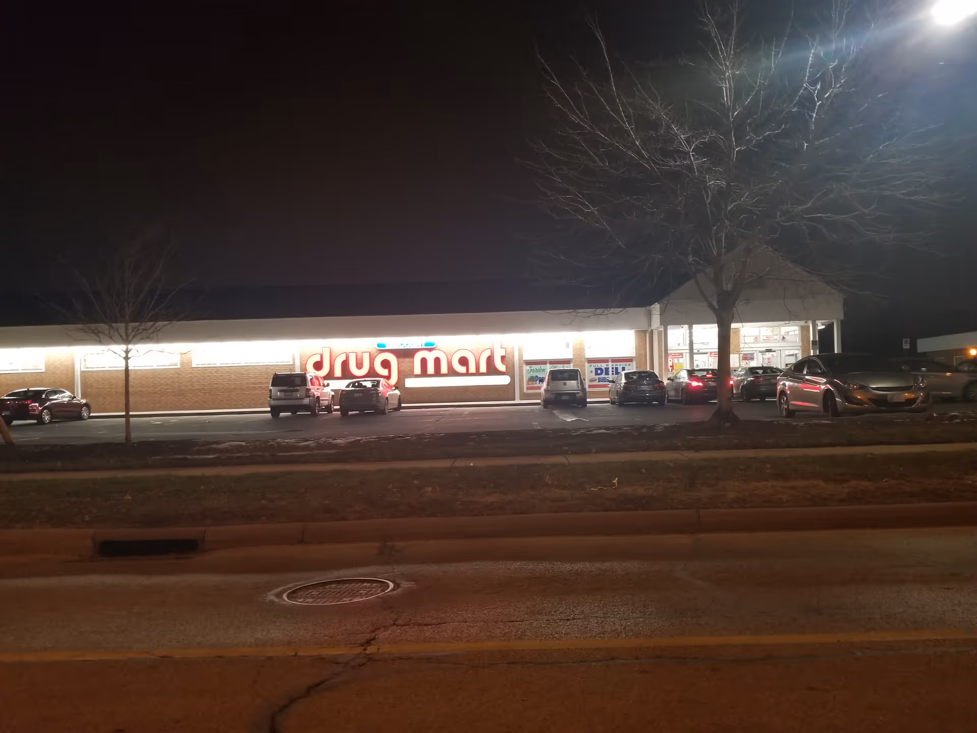 Nighttime exterior of Discount Drug Mart with parked cars and lit store sign.