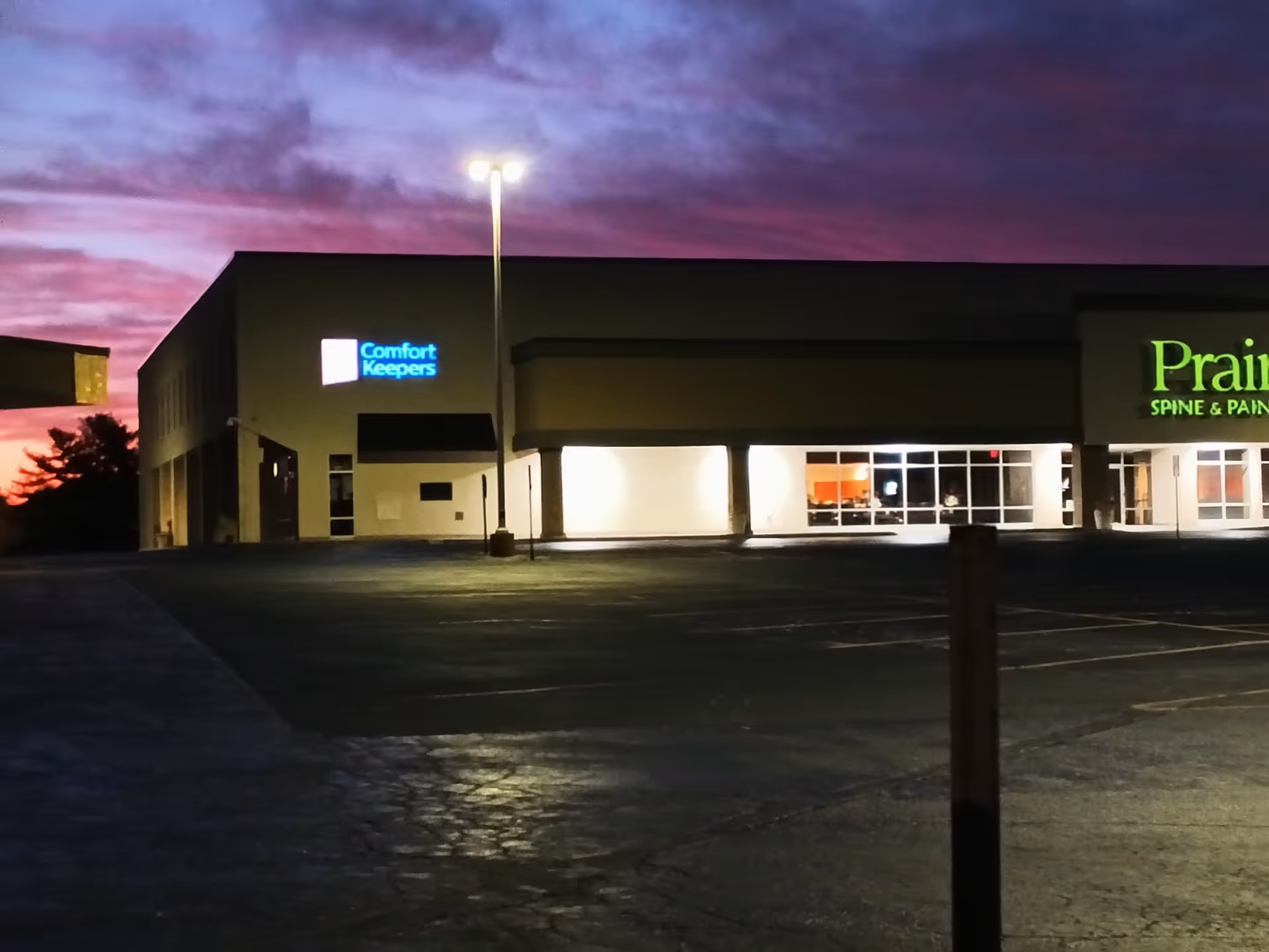 Exterior view of a Comfort Keepers building at dusk with a lit storefront and parking lot.