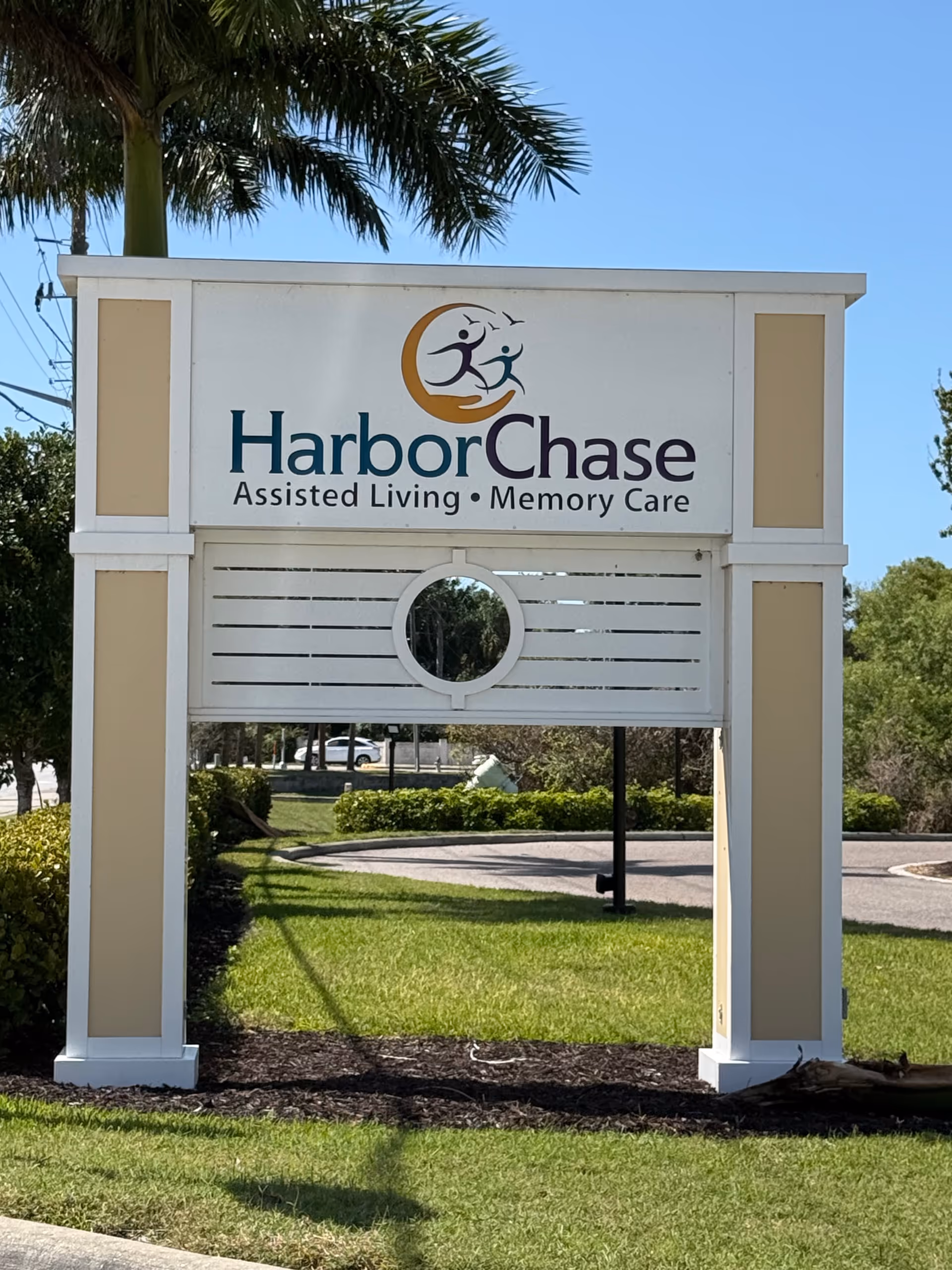 HarborChase Assisted Living sign sits on a lawn with palm trees.