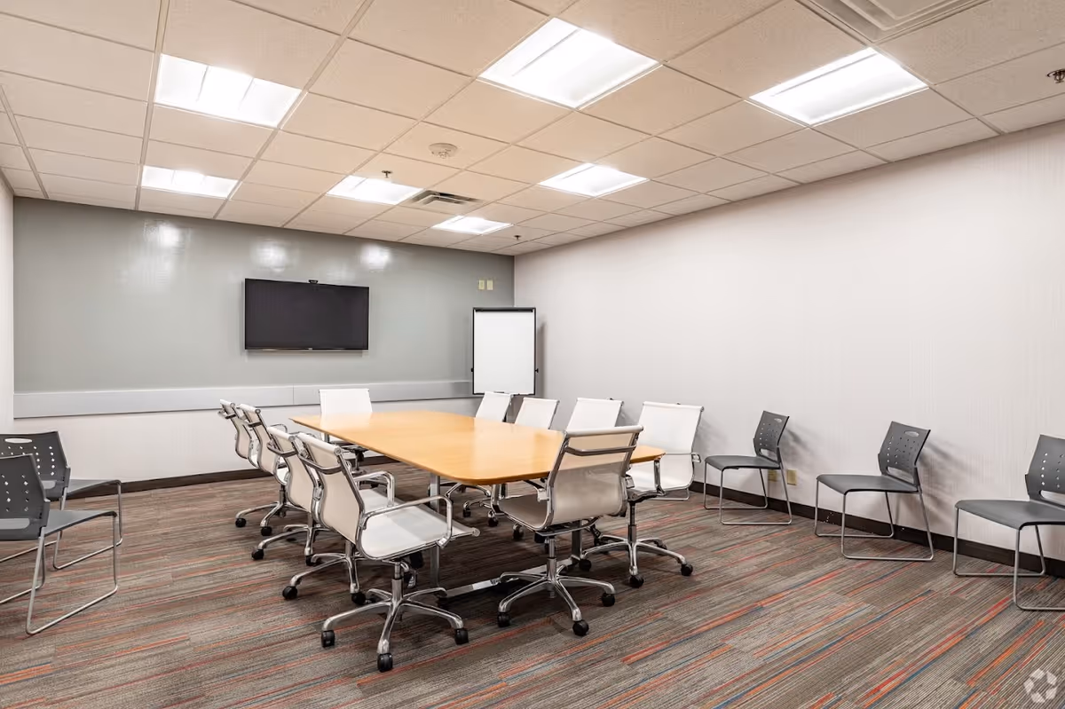 Empty conference room with a long wooden table, white chairs, and a wall-mounted TV.