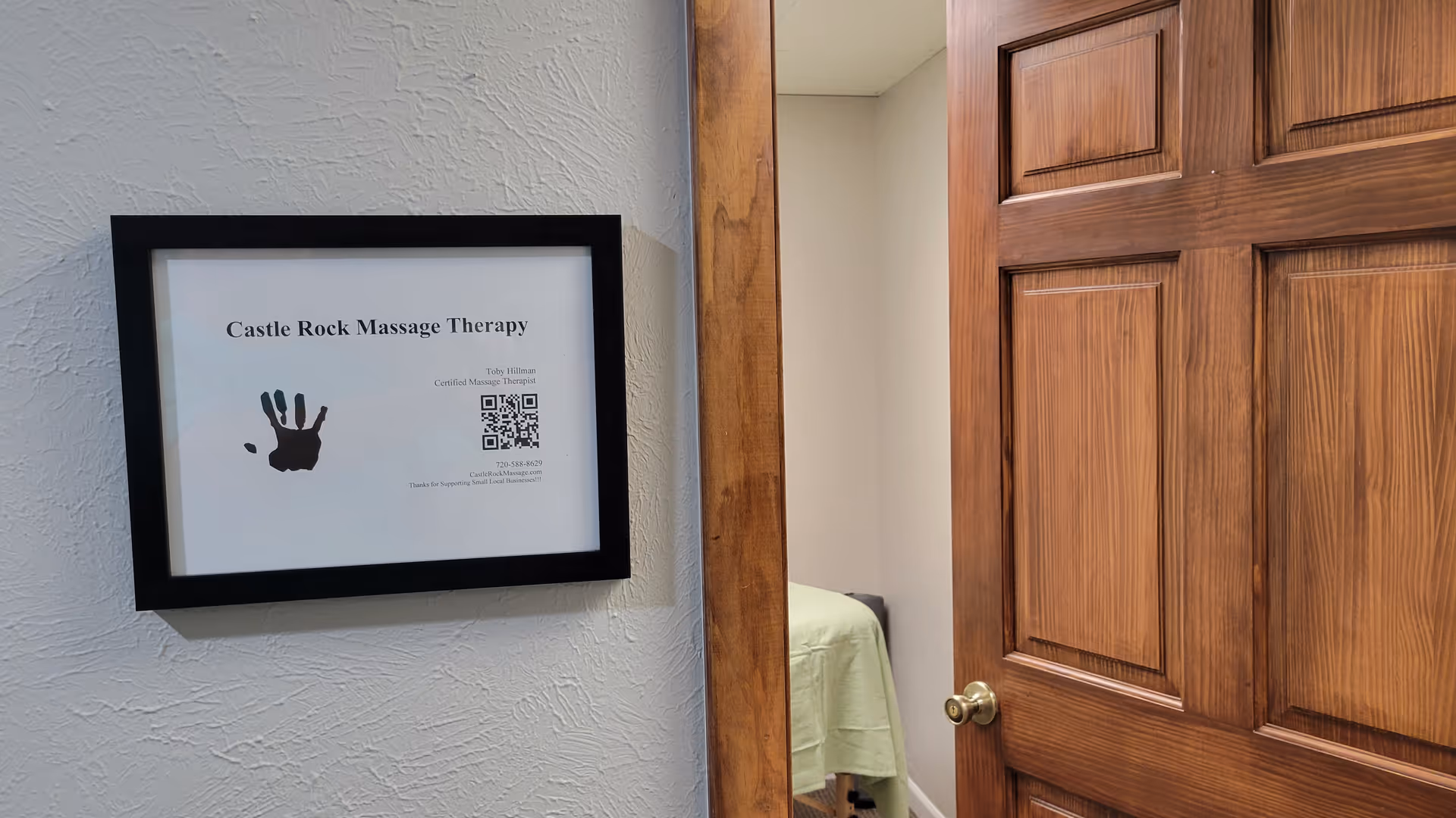 Framed sign reading Castle Rock Massage Therapy hangs on a textured wall beside a wooden door