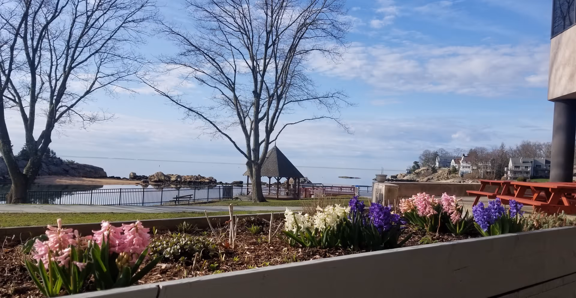 Outdoor area with flowering planters, trees, gazebo, and water view.