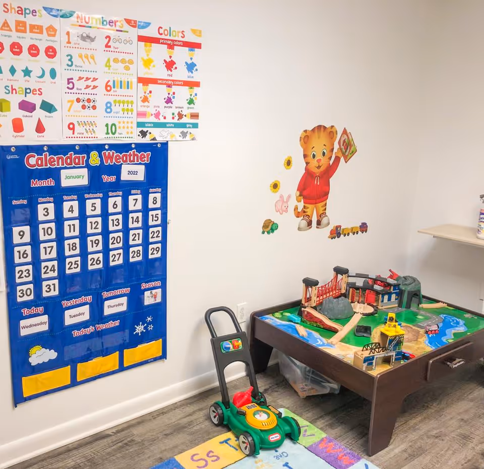 Bright children's play corner with posters, calendar charts, and a toy train table.