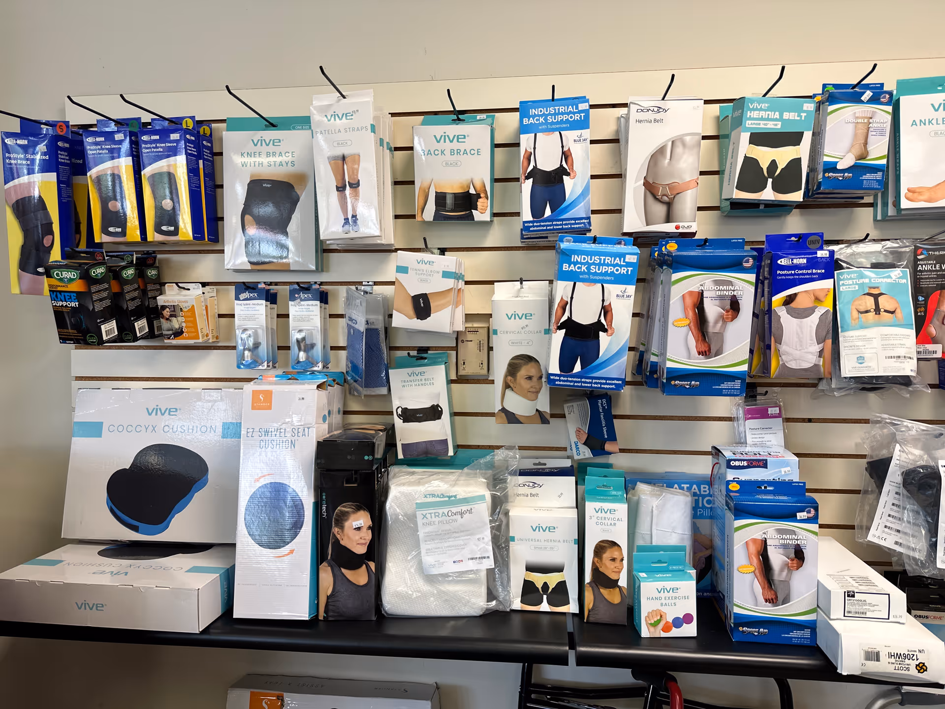 Retail-style wall display featuring assorted braces, back supports, cushions, and other medical mobility aids.