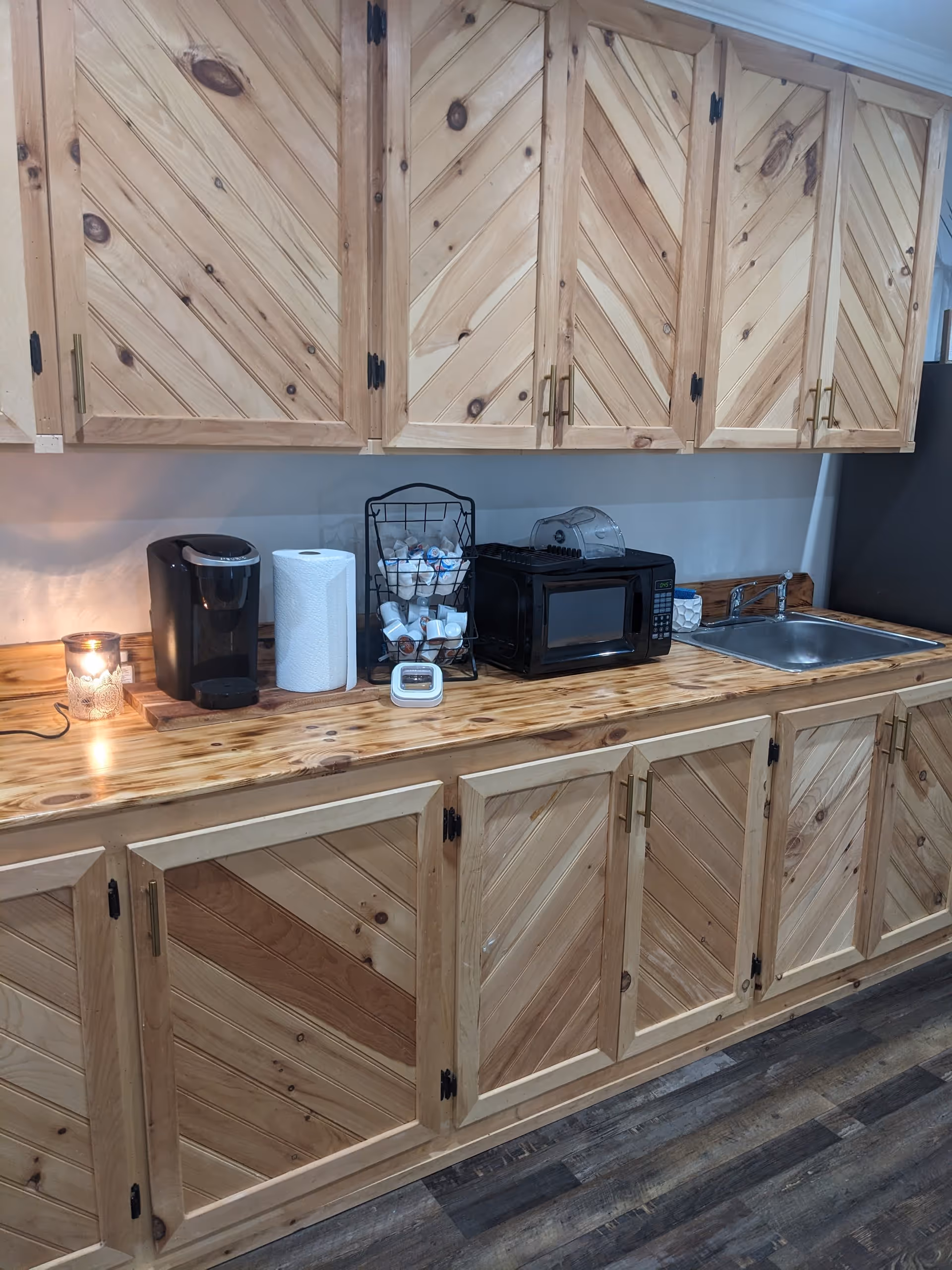 Wooden cabinets line a kitchenette with coffee maker, microwave, toaster, sink, and paper towels.