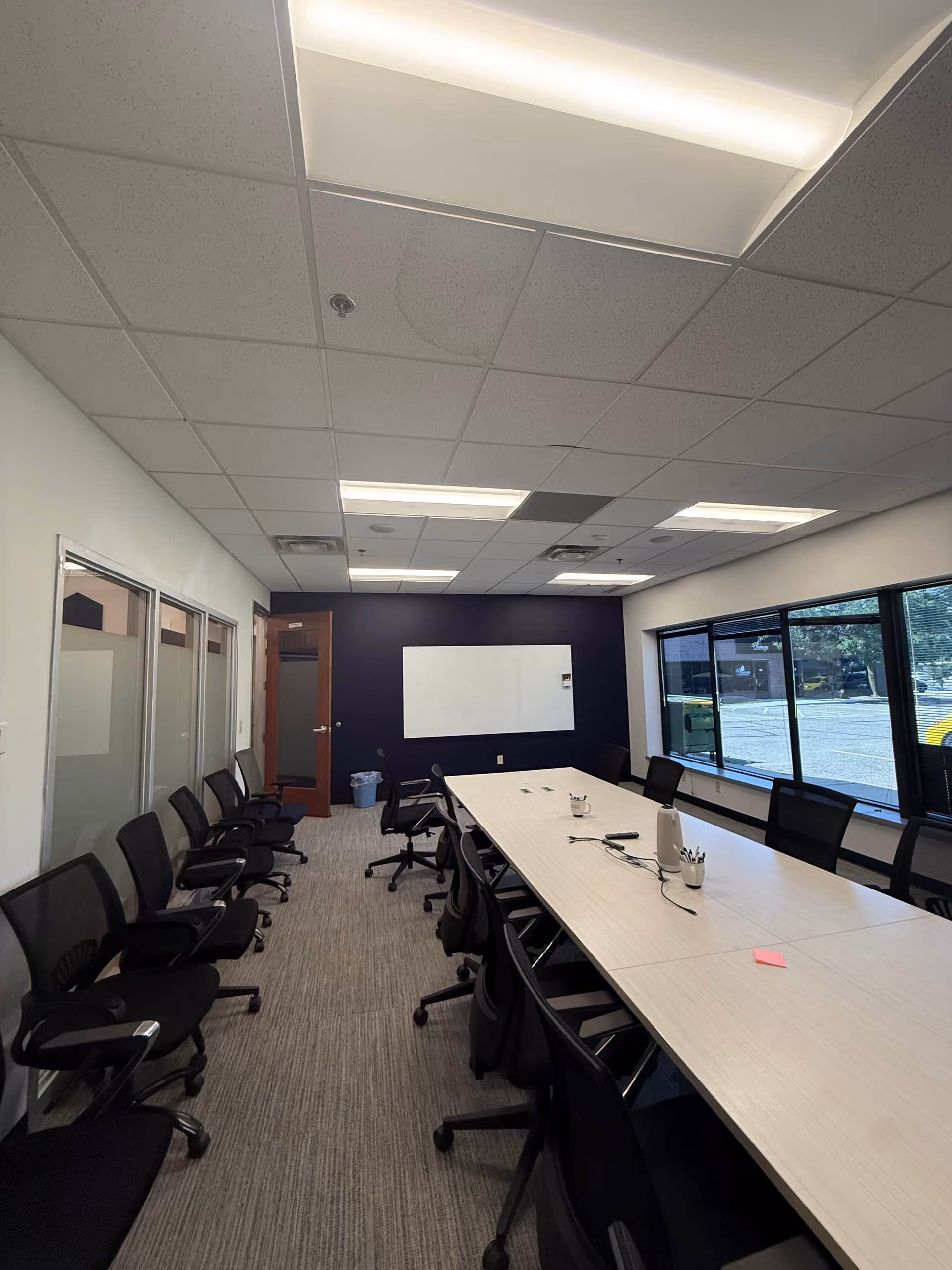 A long conference table with chairs around in a bright meeting room with a whiteboard.