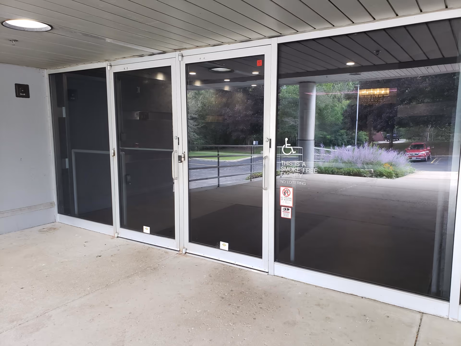 Glass entrance doors of a hospice facility with wheelchair signage and exterior landscaping visible.