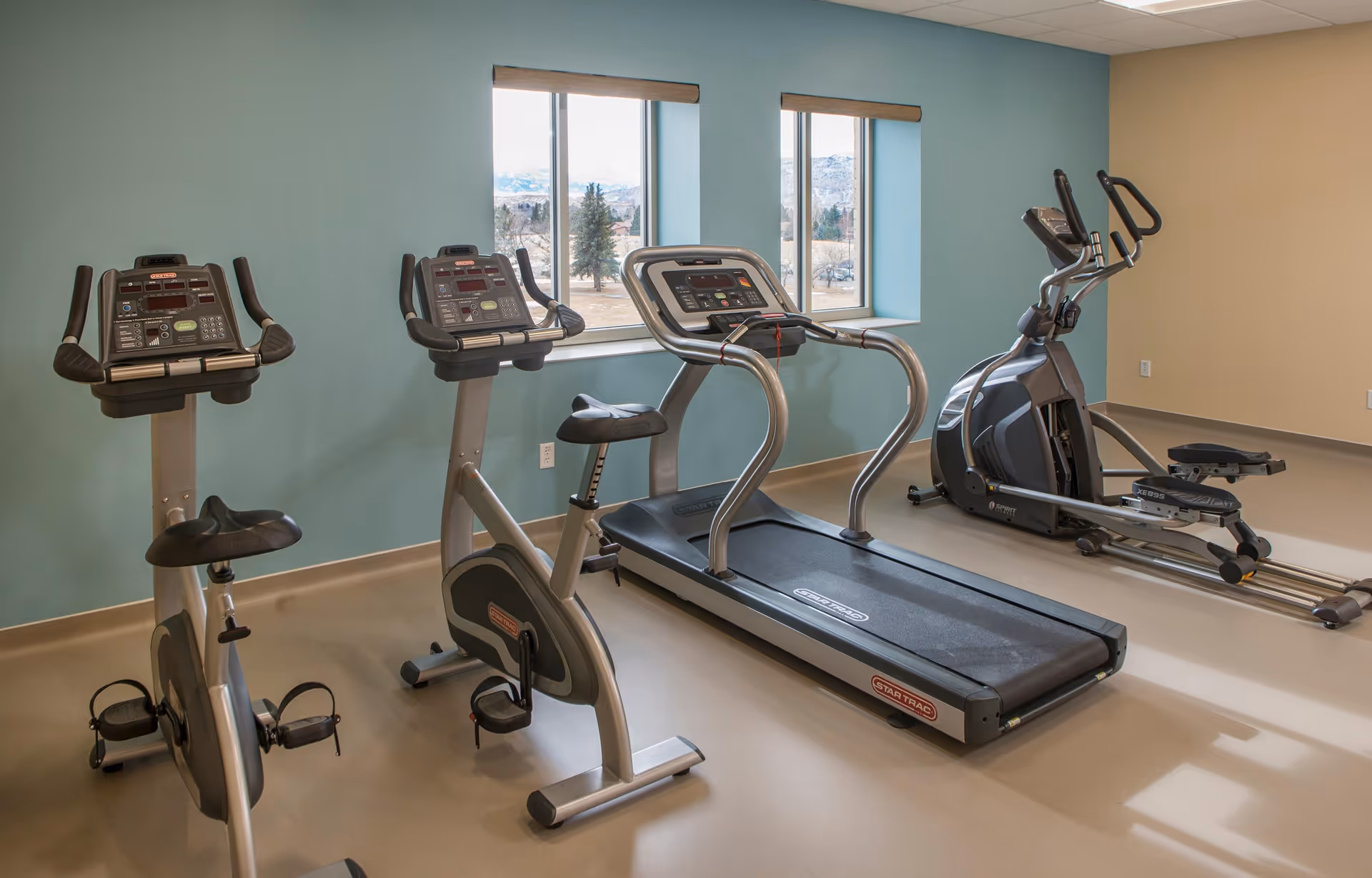 Bright interior fitness room with treadmills, stationary bikes, and an elliptical machine.