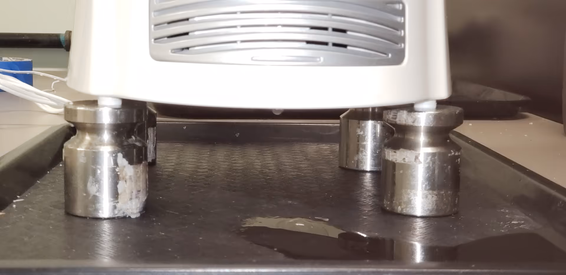 A white appliance on metal caster legs sits above a dark counter with a liquid spill.