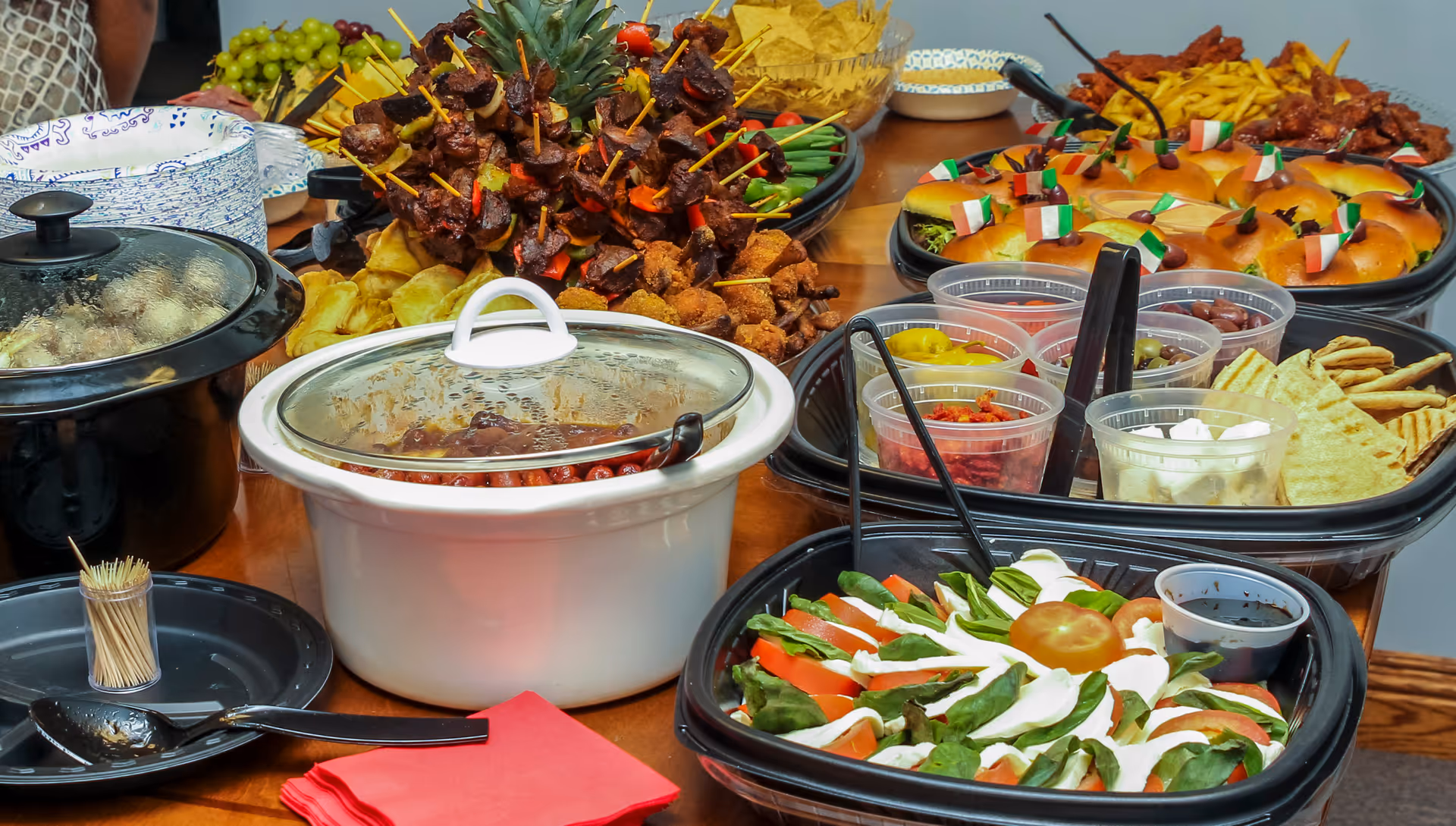 An indoor dining buffet with various dishes, salads, and skewered appetizers on a wooden table.