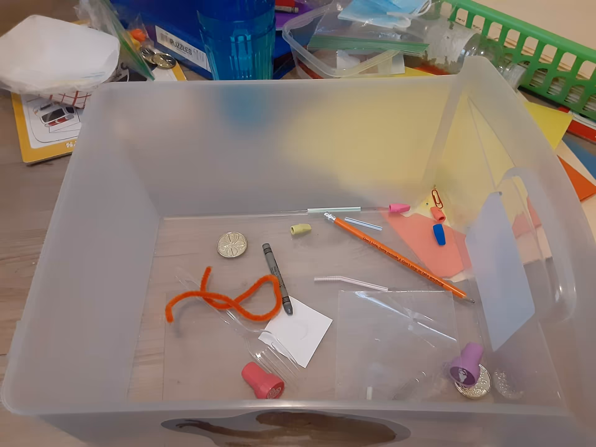 Clear plastic bin on a desk filled with craft supplies and small tools.