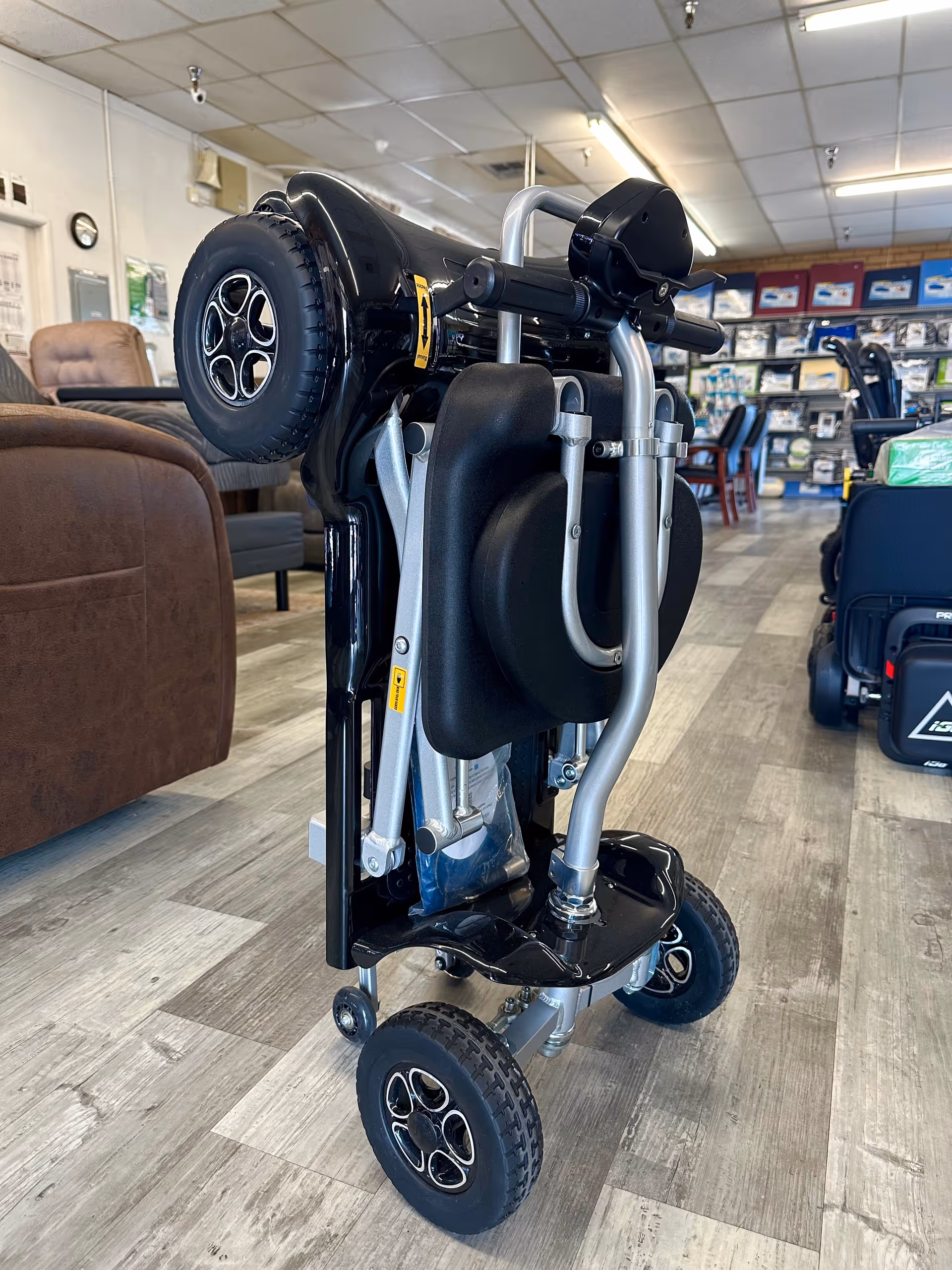 Foldable mobility scooter displayed inside a showroom with chairs and medical supply shelves.