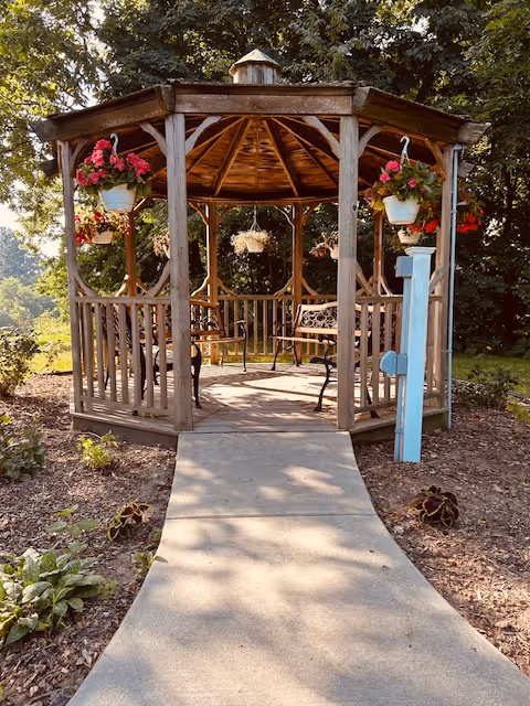 A wooden gazebo with hanging planters sits at end of a concrete walkway.