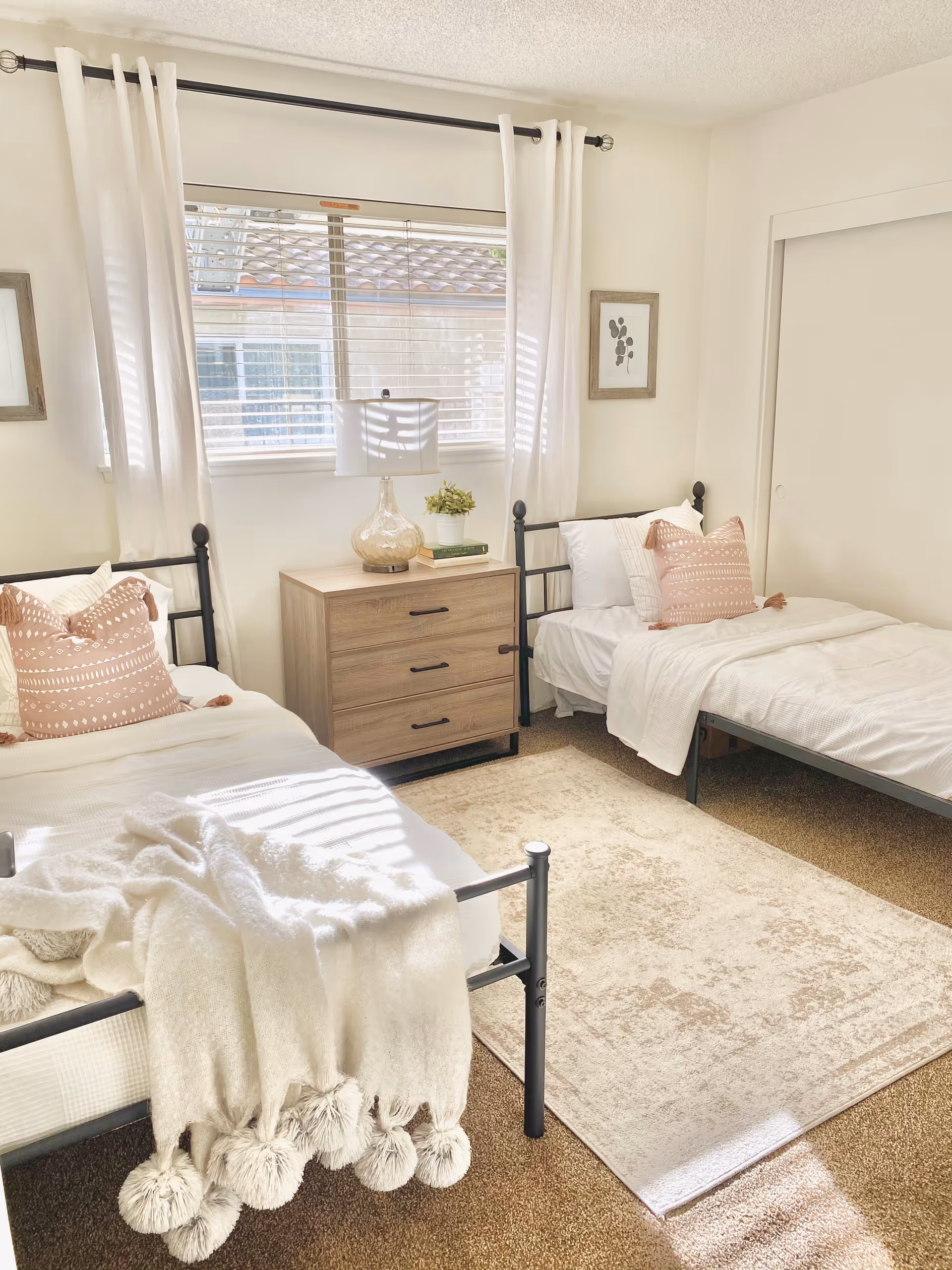 Two single beds with white bedding flank a wooden dresser in a bright bedroom.