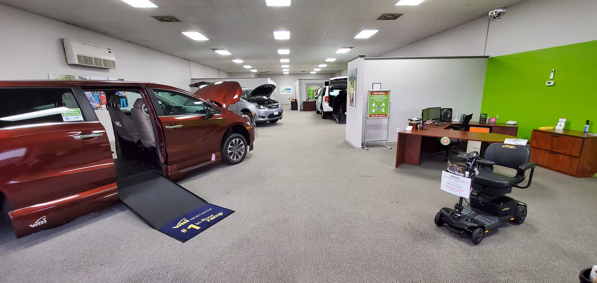 Inside a MobilityWorks showroom, a red minivan with ramp deployed and a scooter nearby.