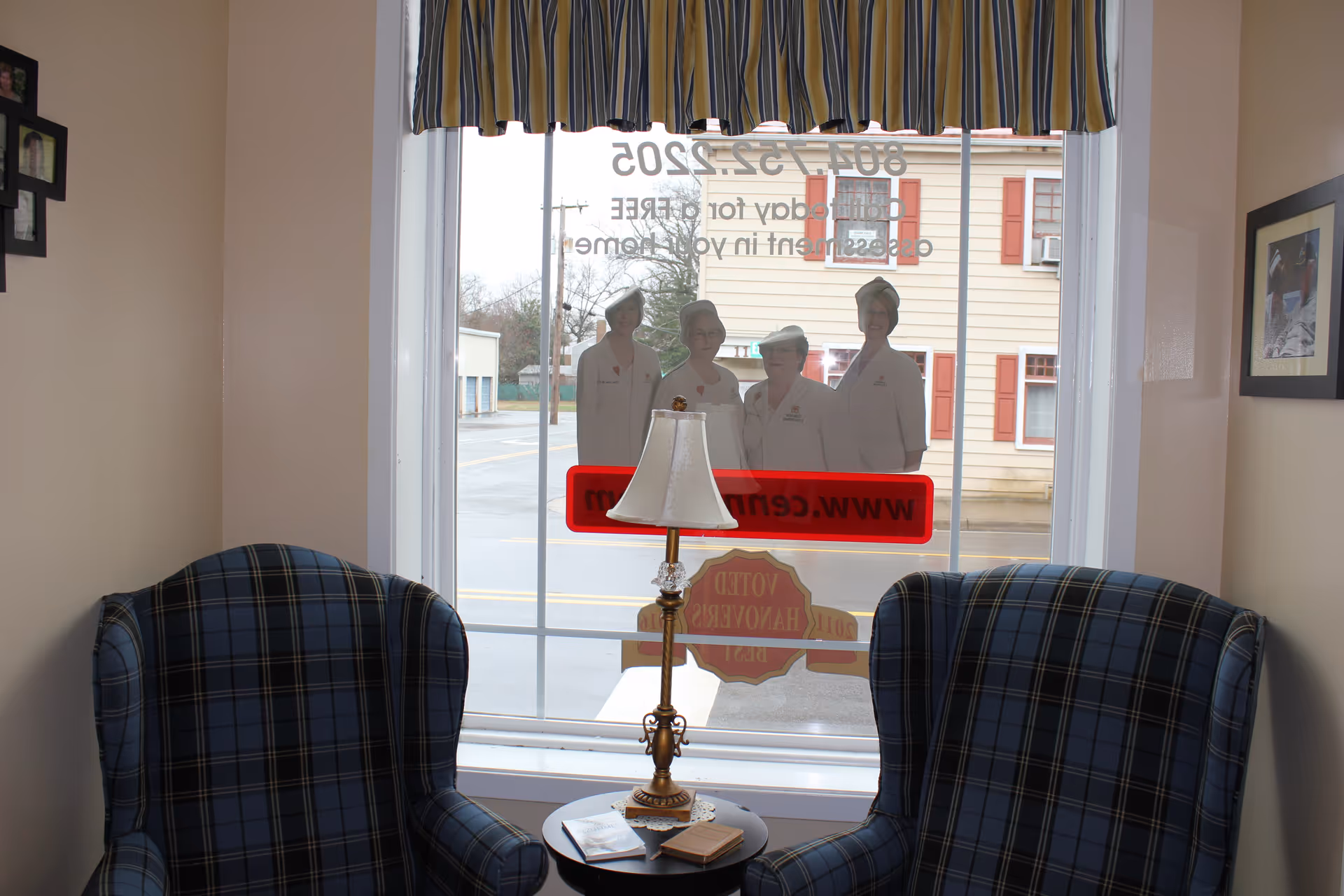 Cozy seating area with plaid armchairs, a lamp, and a window view of the street.
