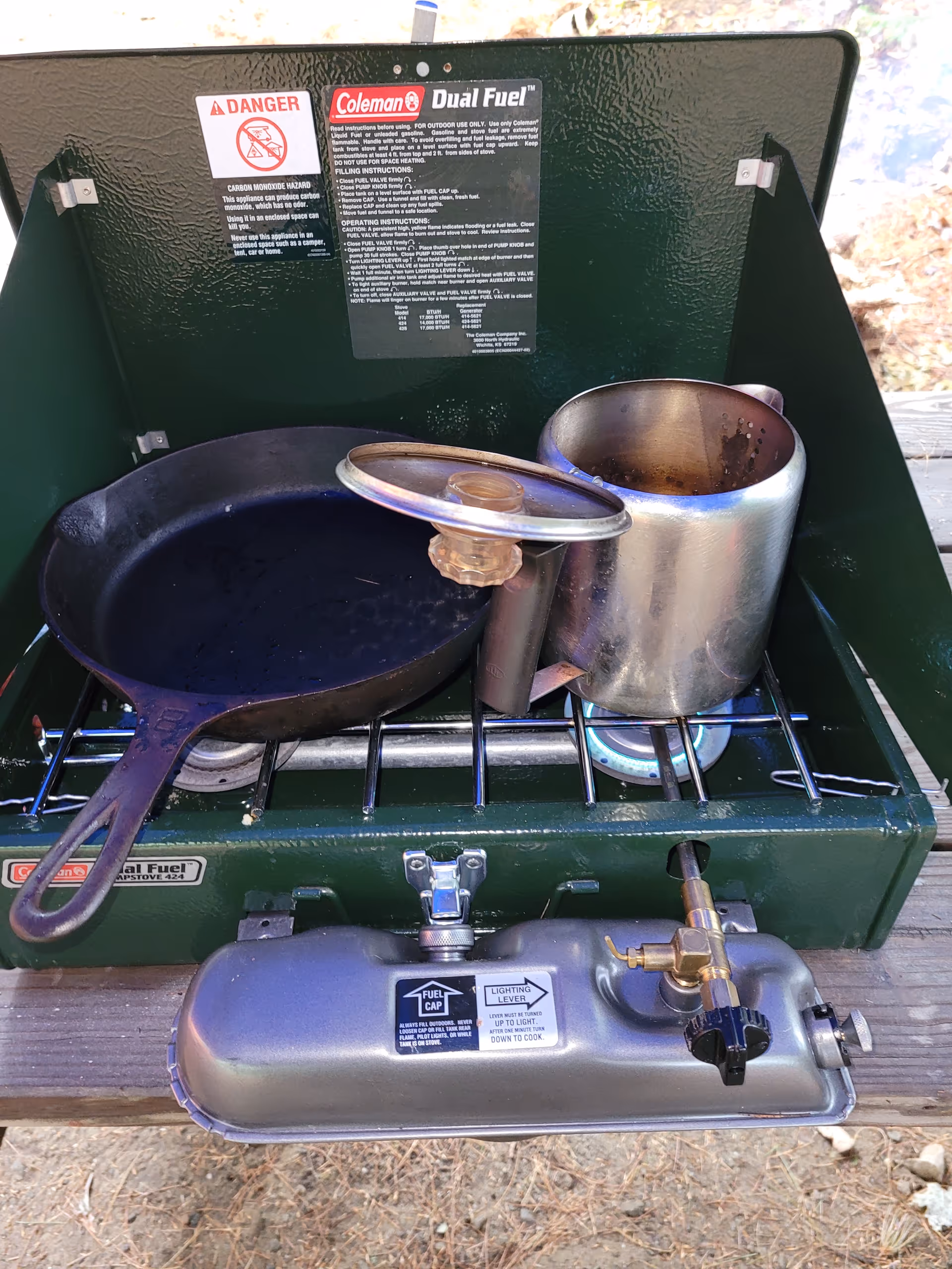 Green outdoor camping stove with pans and pots on a wooden surface.