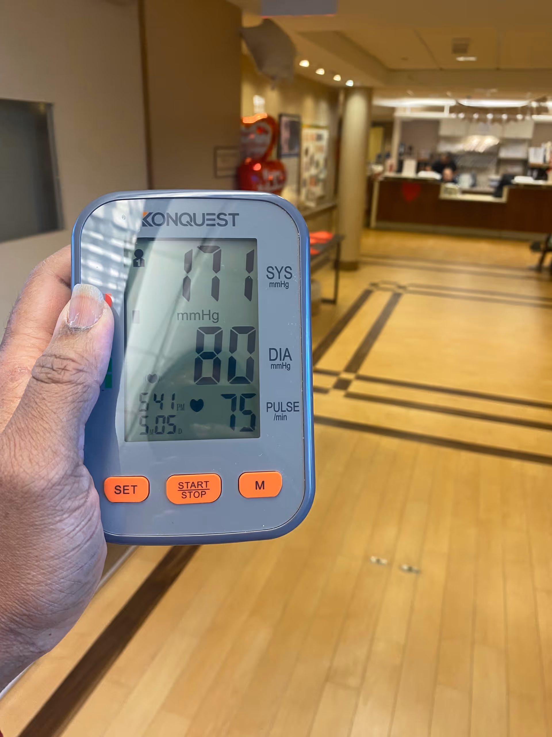 Handheld blood pressure monitor in a senior living facility hallway.