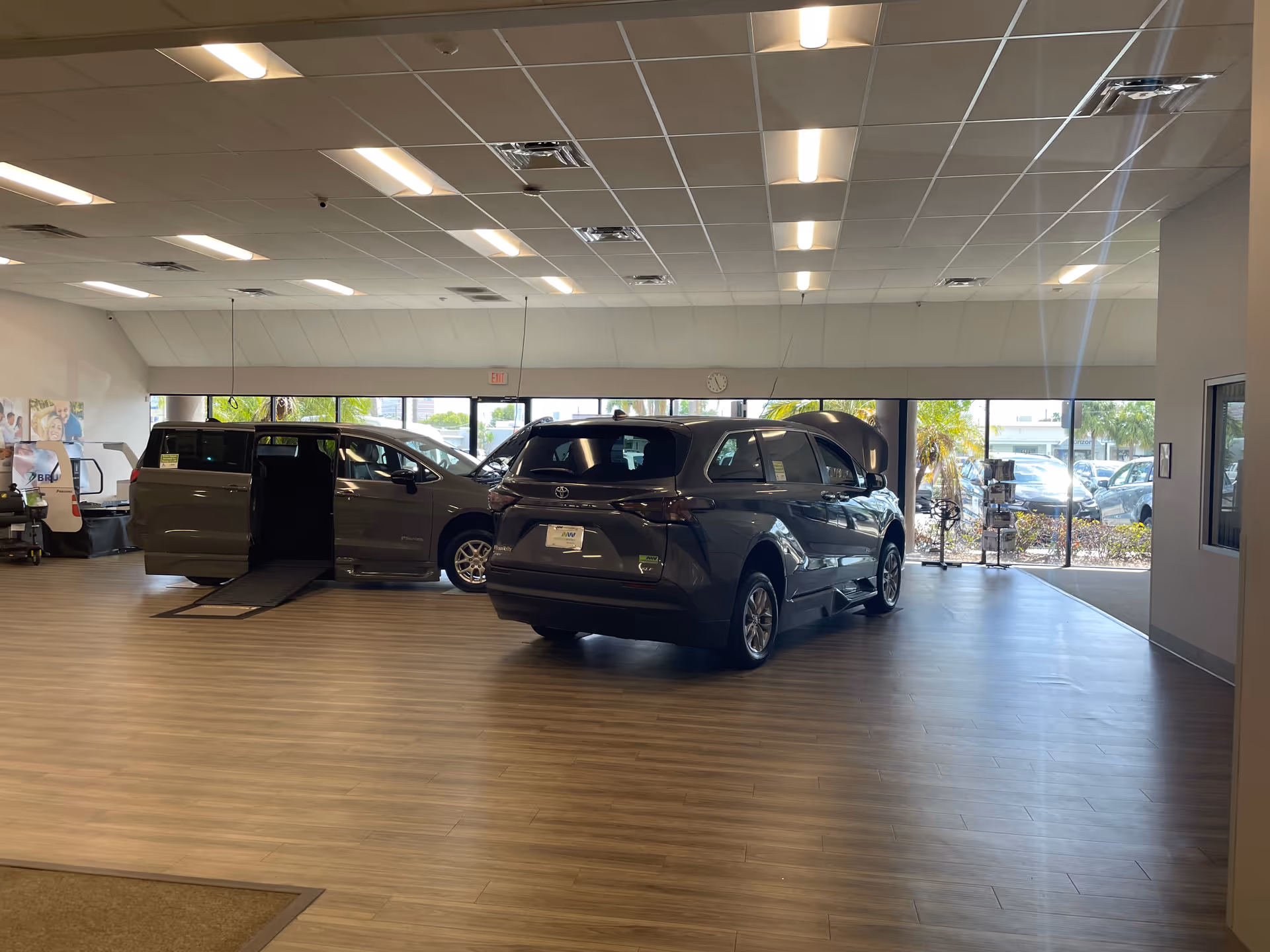 Indoor showroom with two gray minivans, one featuring a ramp, near large windows.