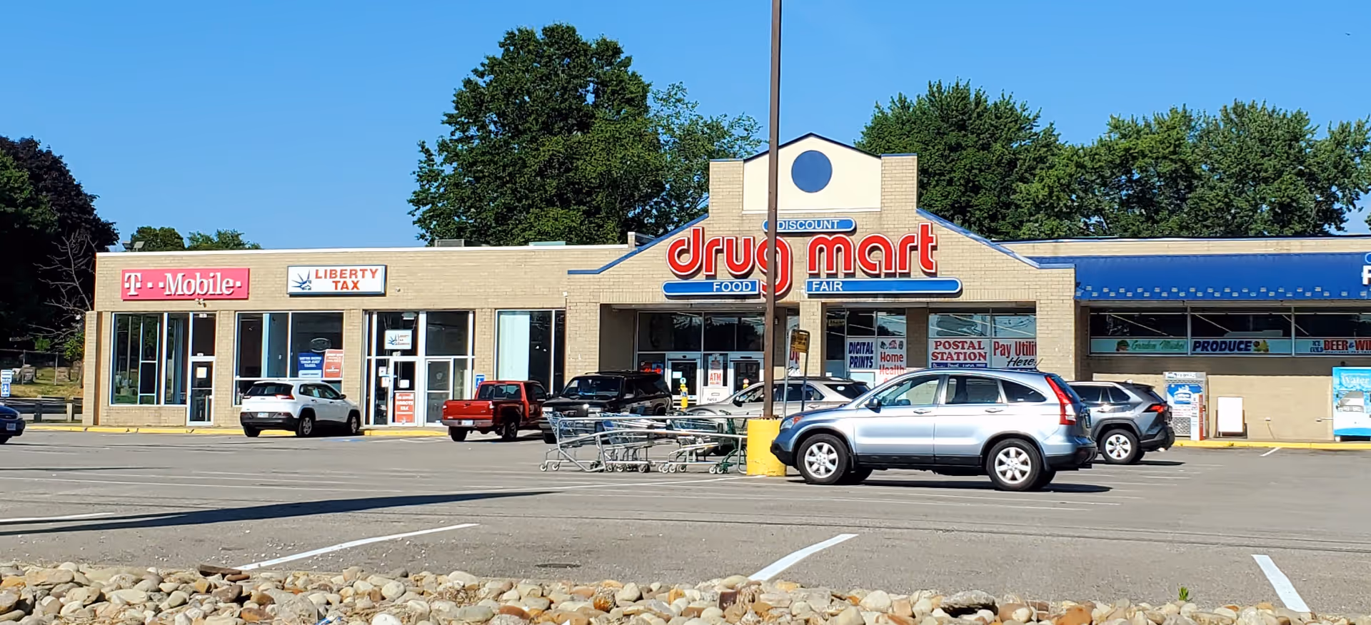 A strip mall with Discount Drug Mart storefronts and parked cars in a parking lot.