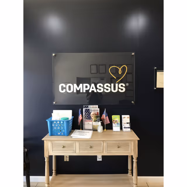 Reception desk beneath a dark wall with a Compassus sign and heart logo.