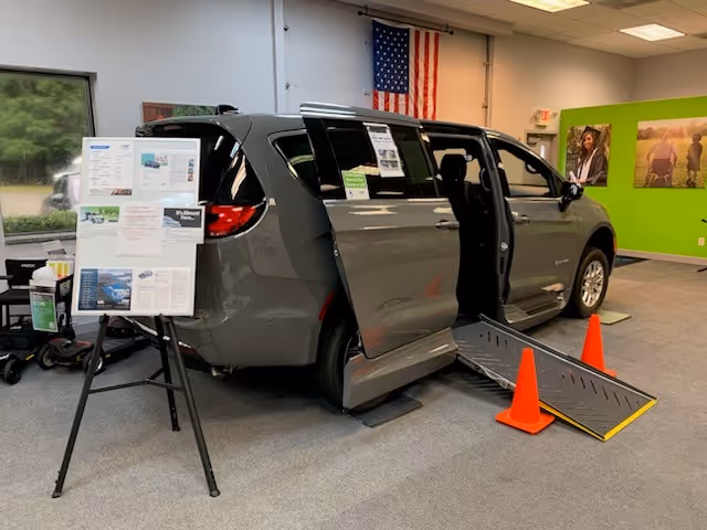 Grey wheelchair accessible van displayed indoors with a ramp and informational boards.