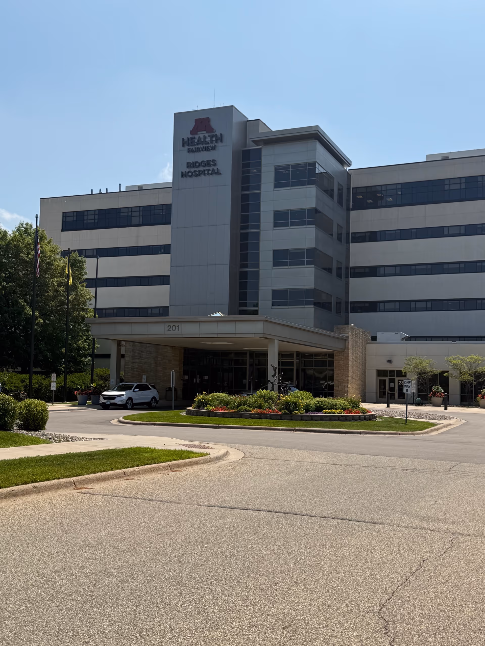 A modern multi-story hospital-like building with a covered entrance and landscaped circle drive.