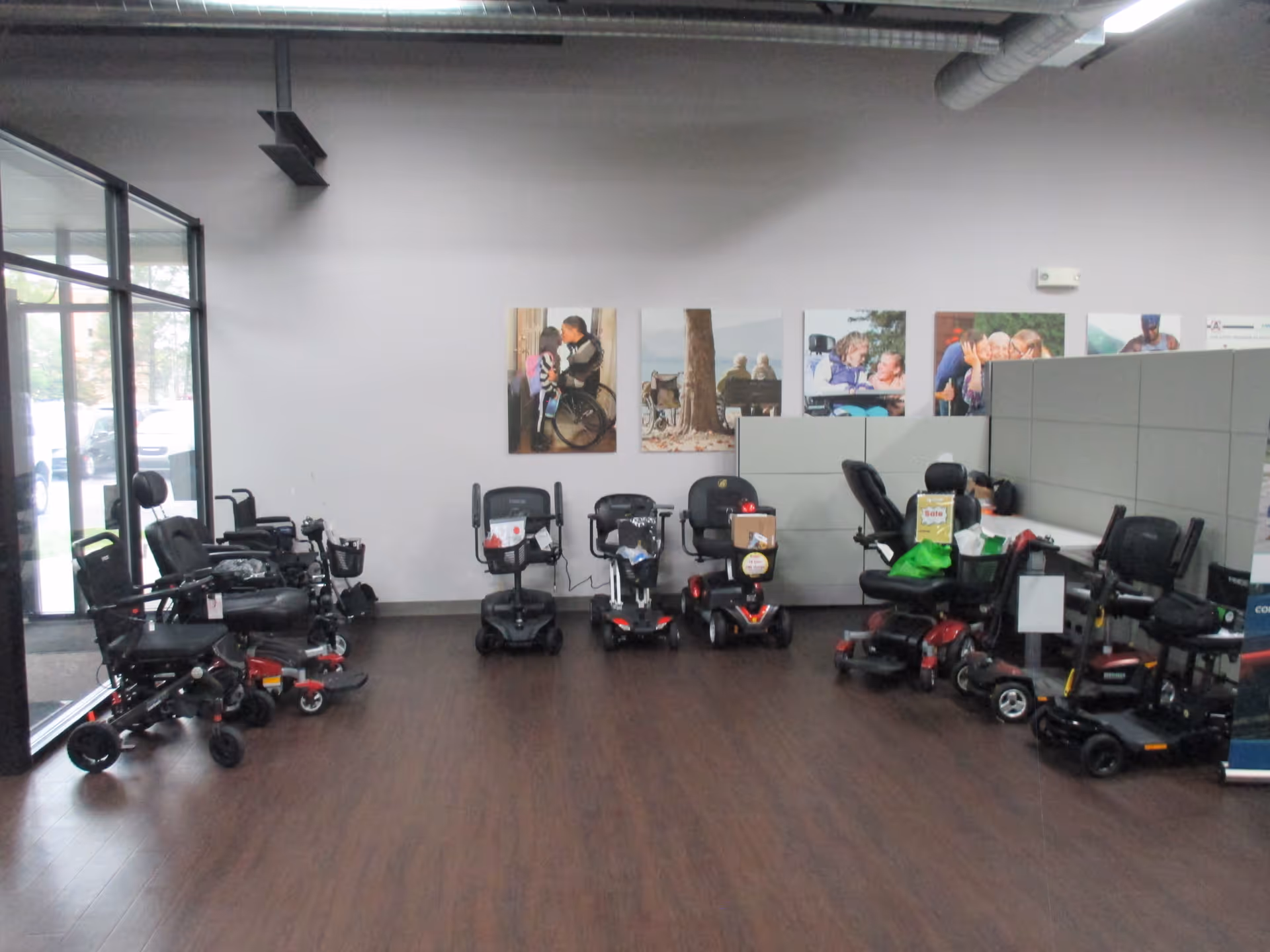 Indoor showroom with multiple mobility scooters lined up along a wall.