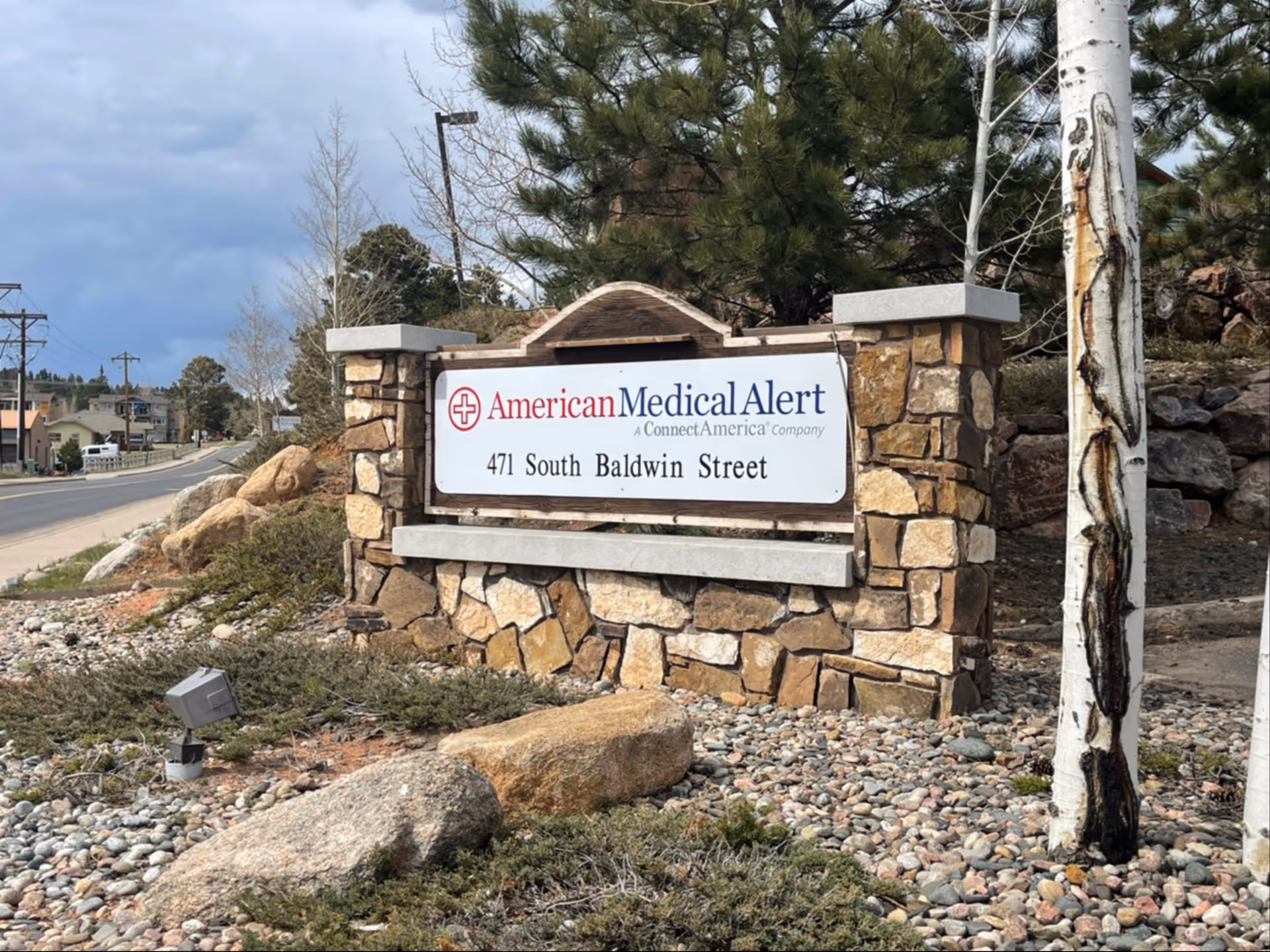 Stone entrance sign for American Medical Alert sits among shrubs and rocks by the street.