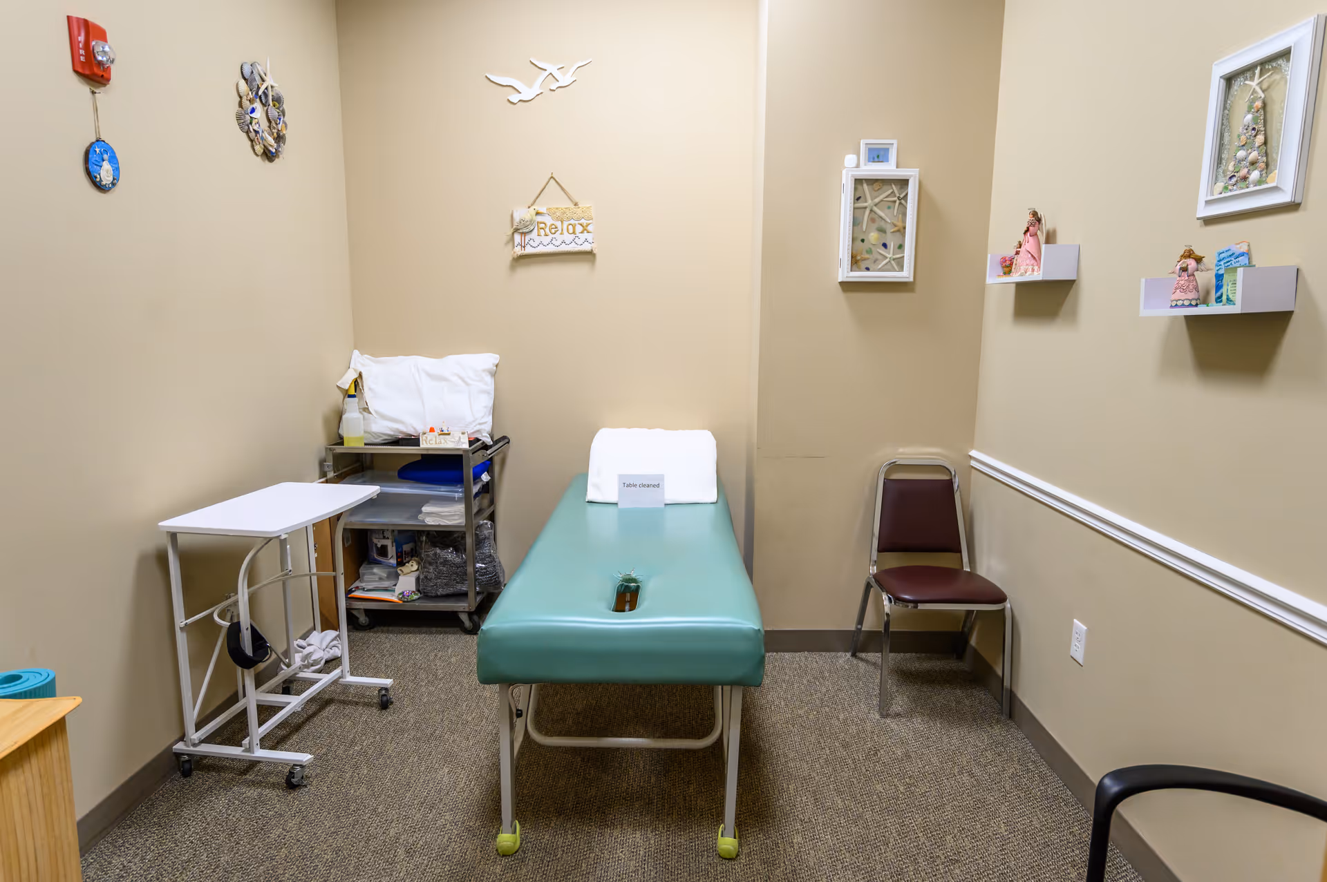 Small beige therapy room with a green examination table and medical cart.