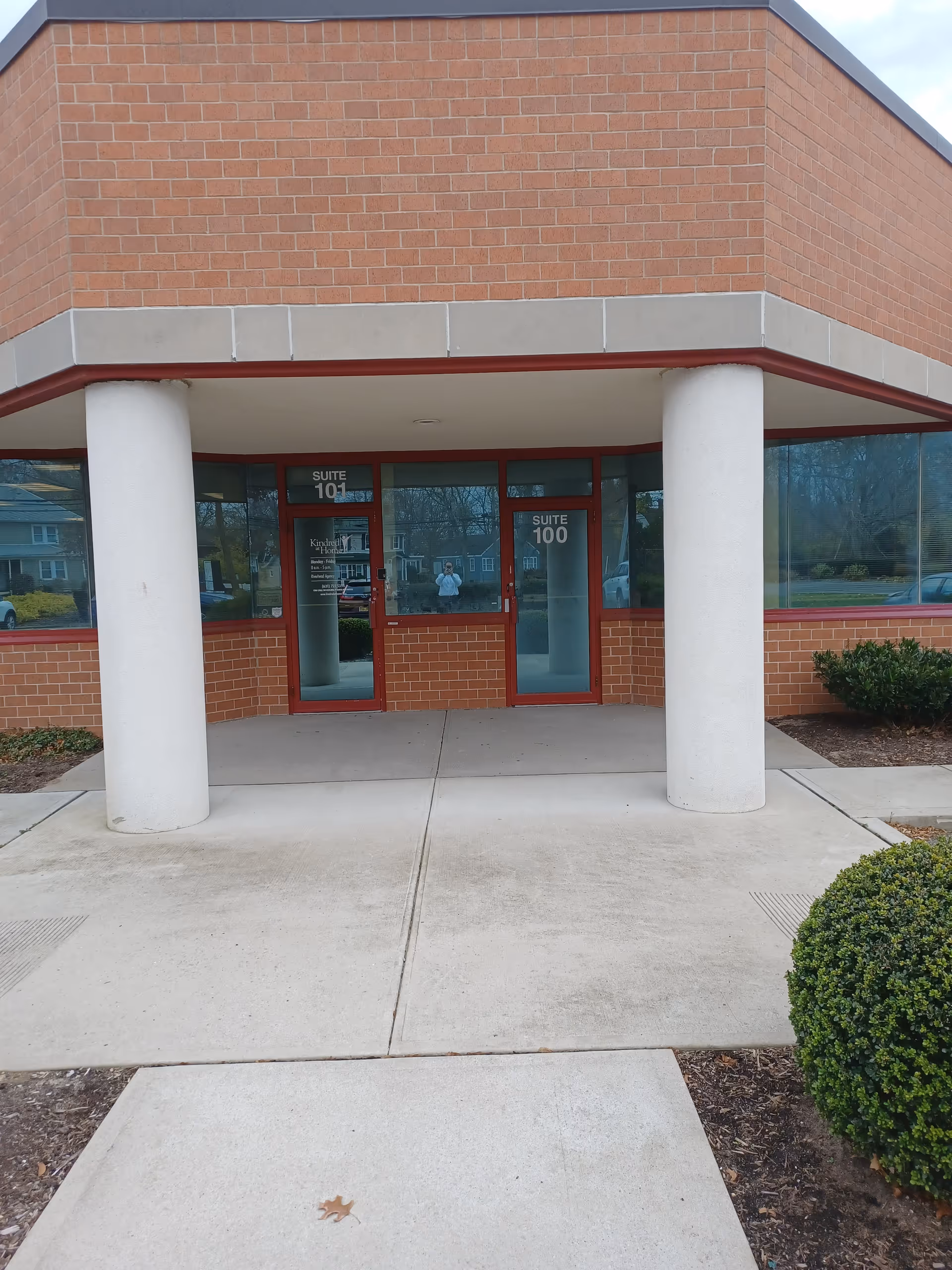 Brick building exterior with glass doors, two white columns, and a covered entrance canopy.