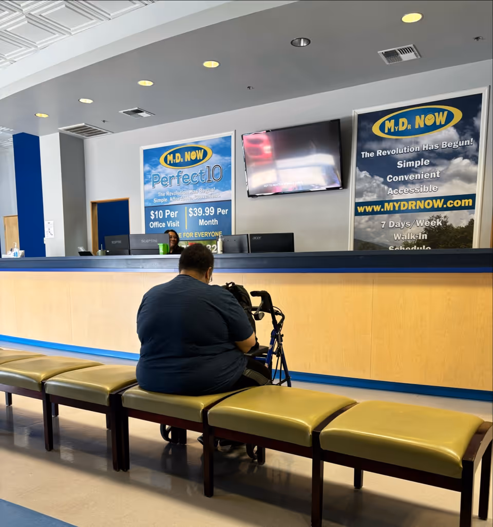 A man with a walker sits on a bench in a clinic lobby.