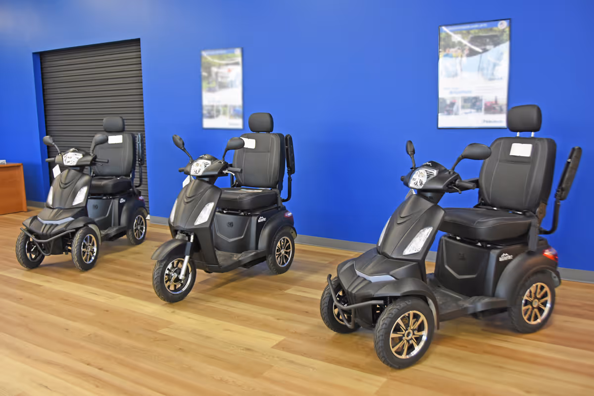 Three black mobility scooters lined up inside a bright blue showroom.