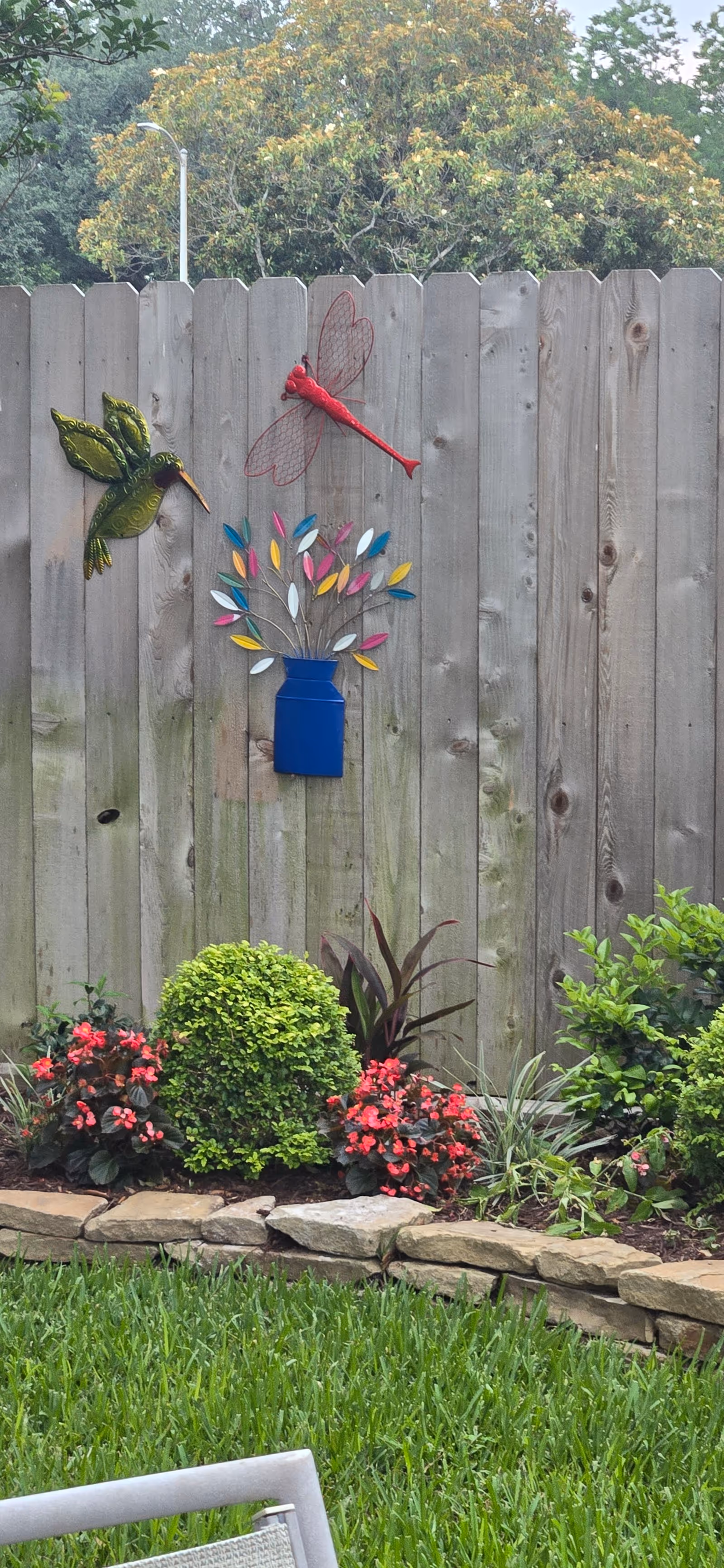 Outdoor garden area with a wooden fence, colorful metal art, and greenery.