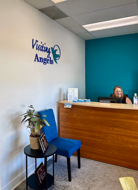 Reception desk in an interior lobby with a teal wall and a smiling receptionist.